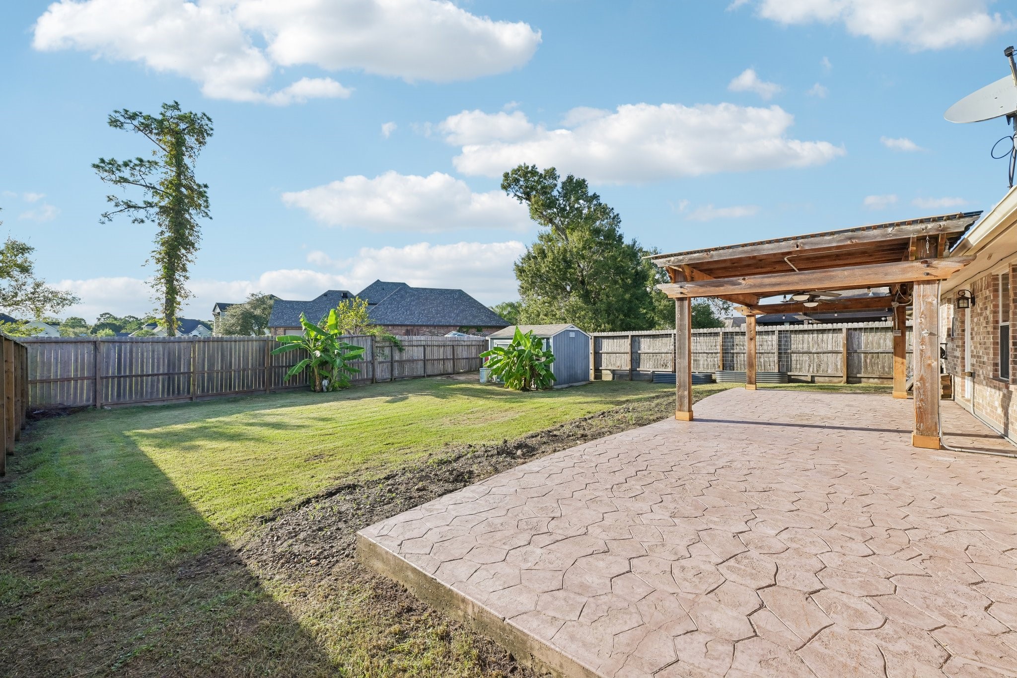 Spacious backyard with a beautifully stamped concrete patio and a wooden pergola, perfect for outdoor gatherings.