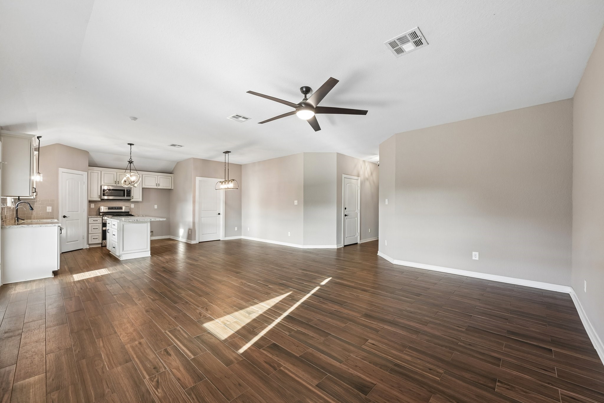 Spacious open-concept living area with elegant wood flooring, modern ceiling fan, and a bright kitchen featuring stainless steel appliances and a central island.