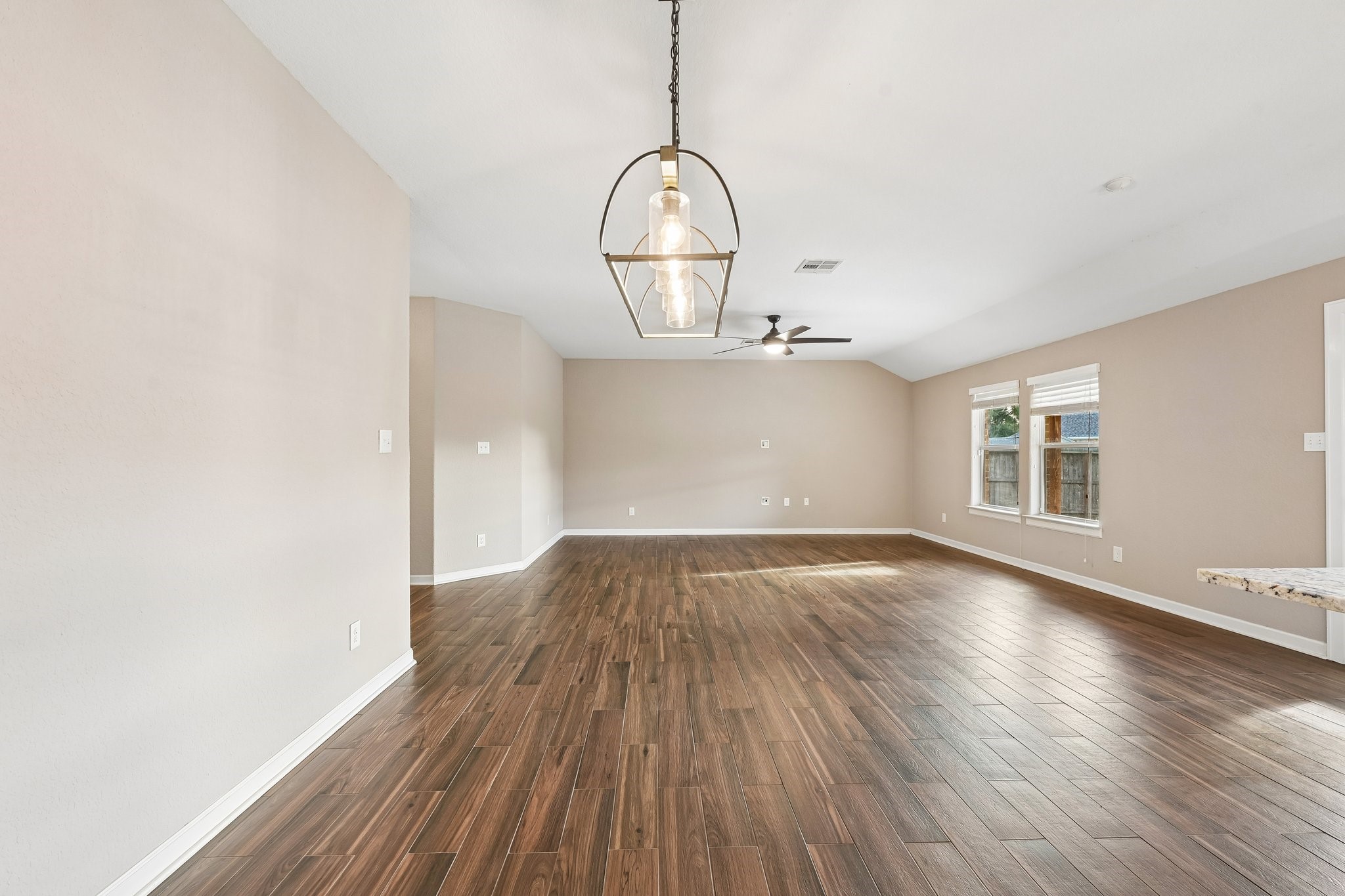Spacious living area with elegant wood flooring, modern light fixture, and abundant natural light from large windows.