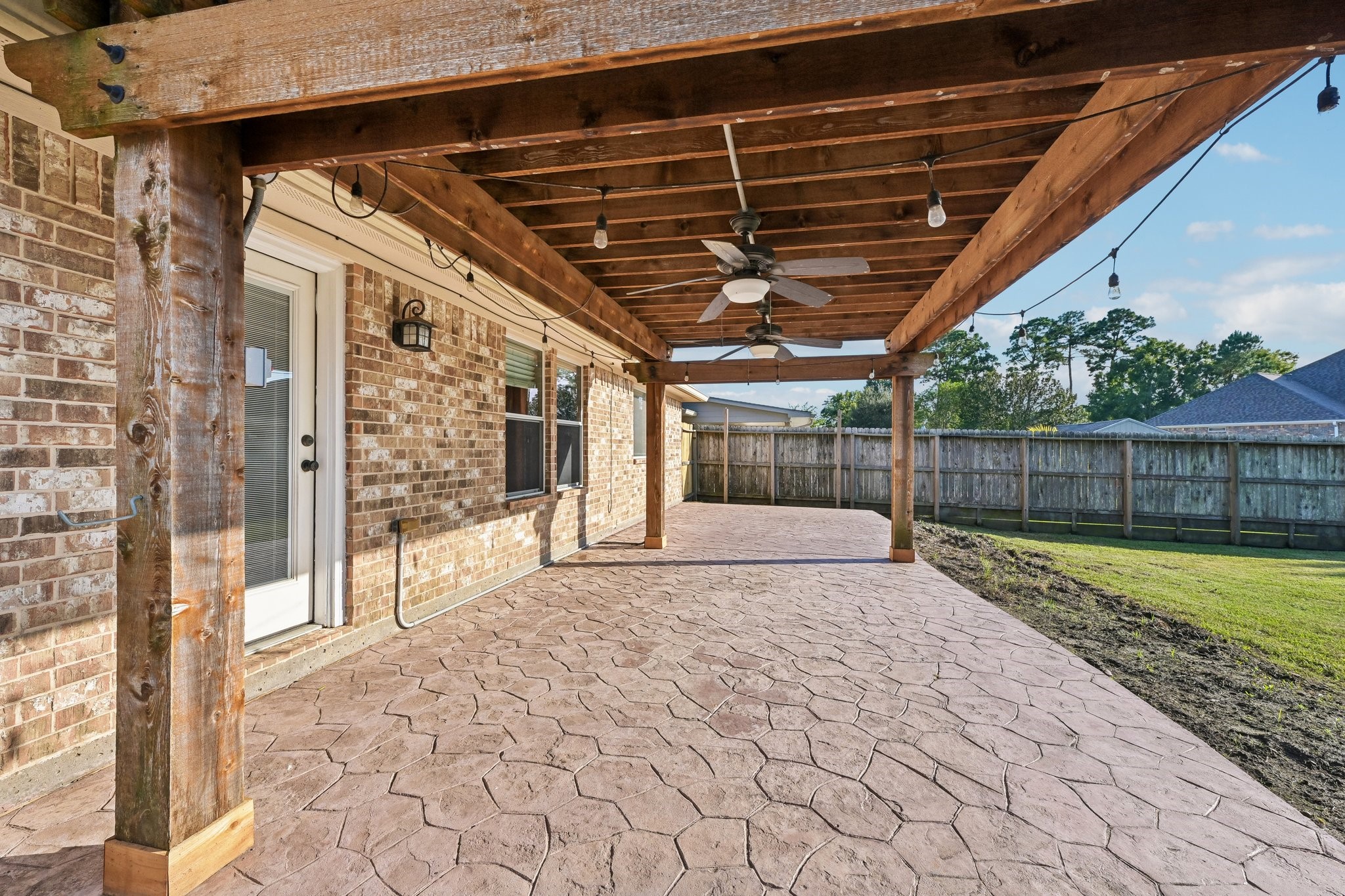 Spacious covered patio with a stylish pergola, perfect for outdoor entertaining, featuring durable stamped concrete flooring and ceiling fans for added comfort.