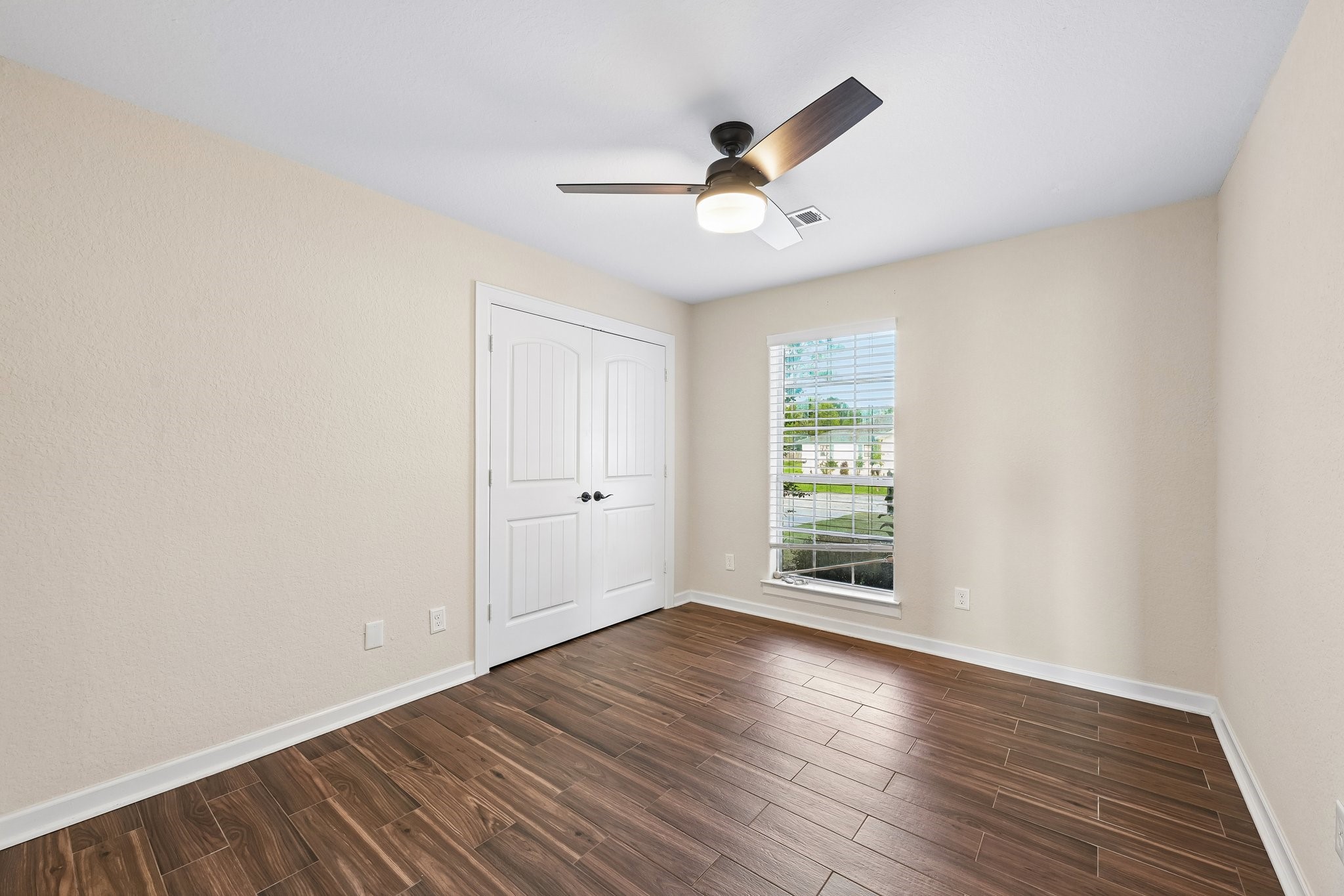 Bright and airy room featuring elegant wood-look tile flooring, a modern ceiling fan, and a large window for natural light.