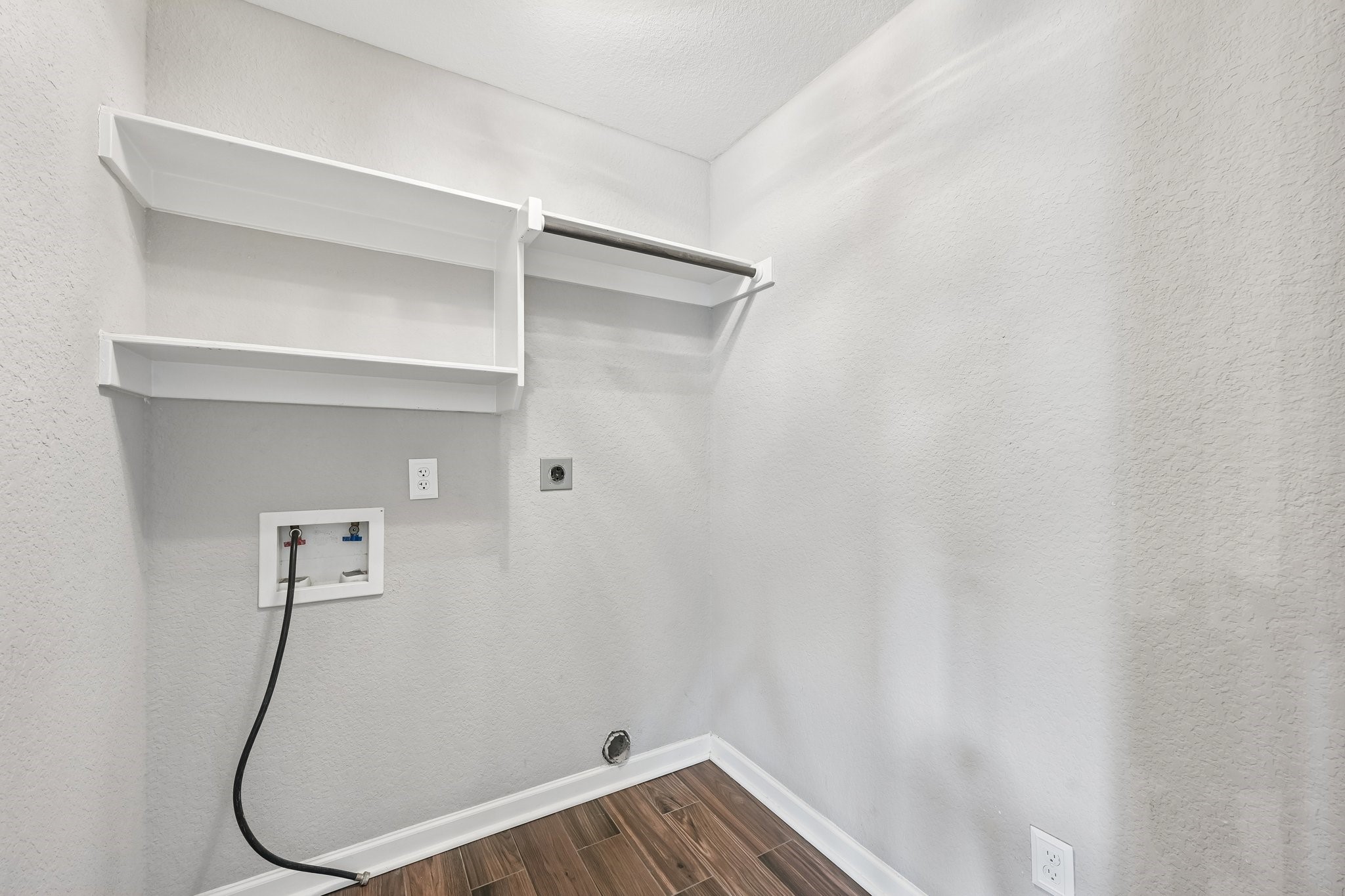 Spacious laundry room with built-in shelves, hookups for washer and dryer, and sleek wood-look tile flooring.