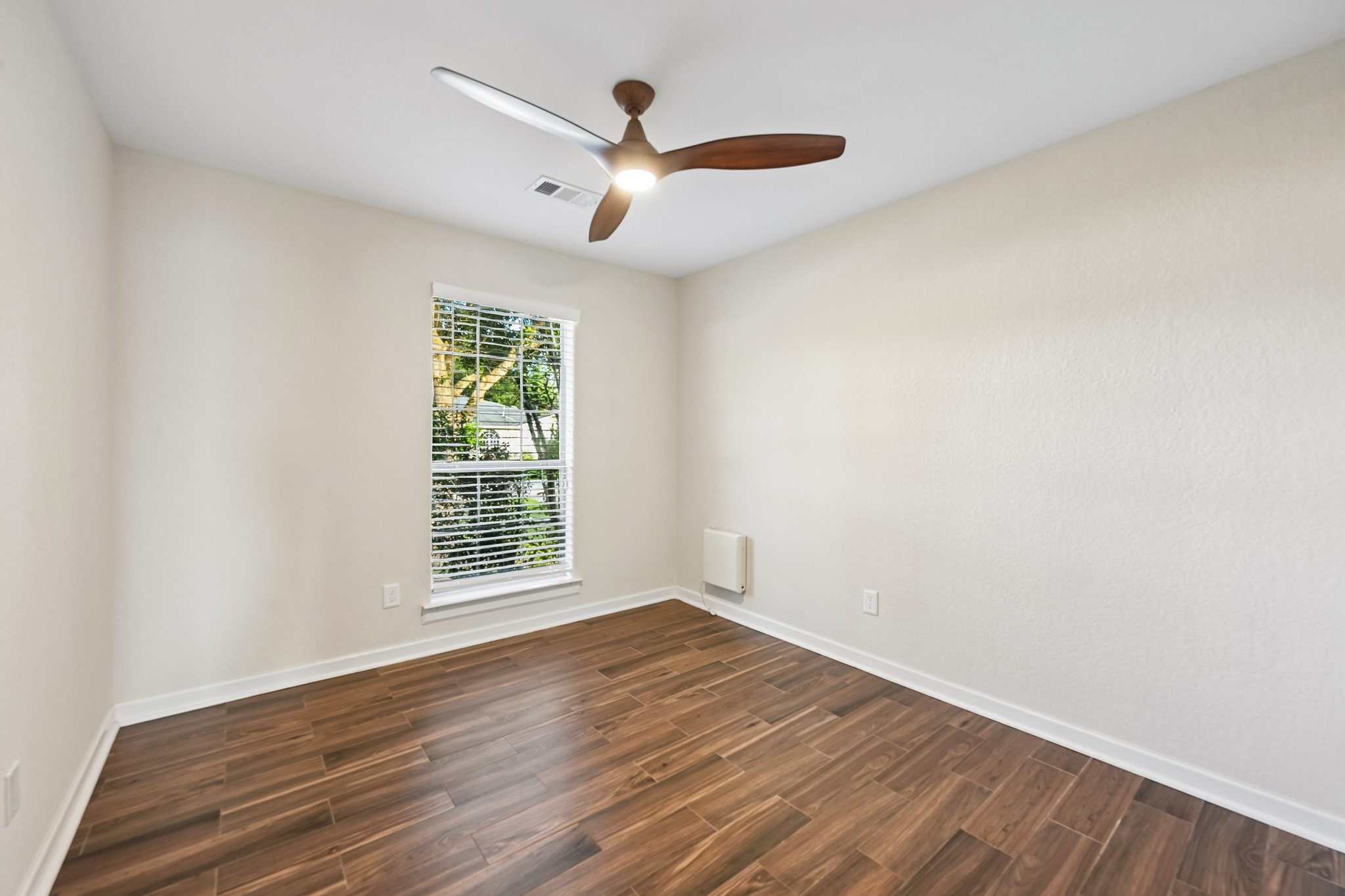 Bright and inviting room with sleek wood flooring, a modern ceiling fan, and a large window providing ample natural light.