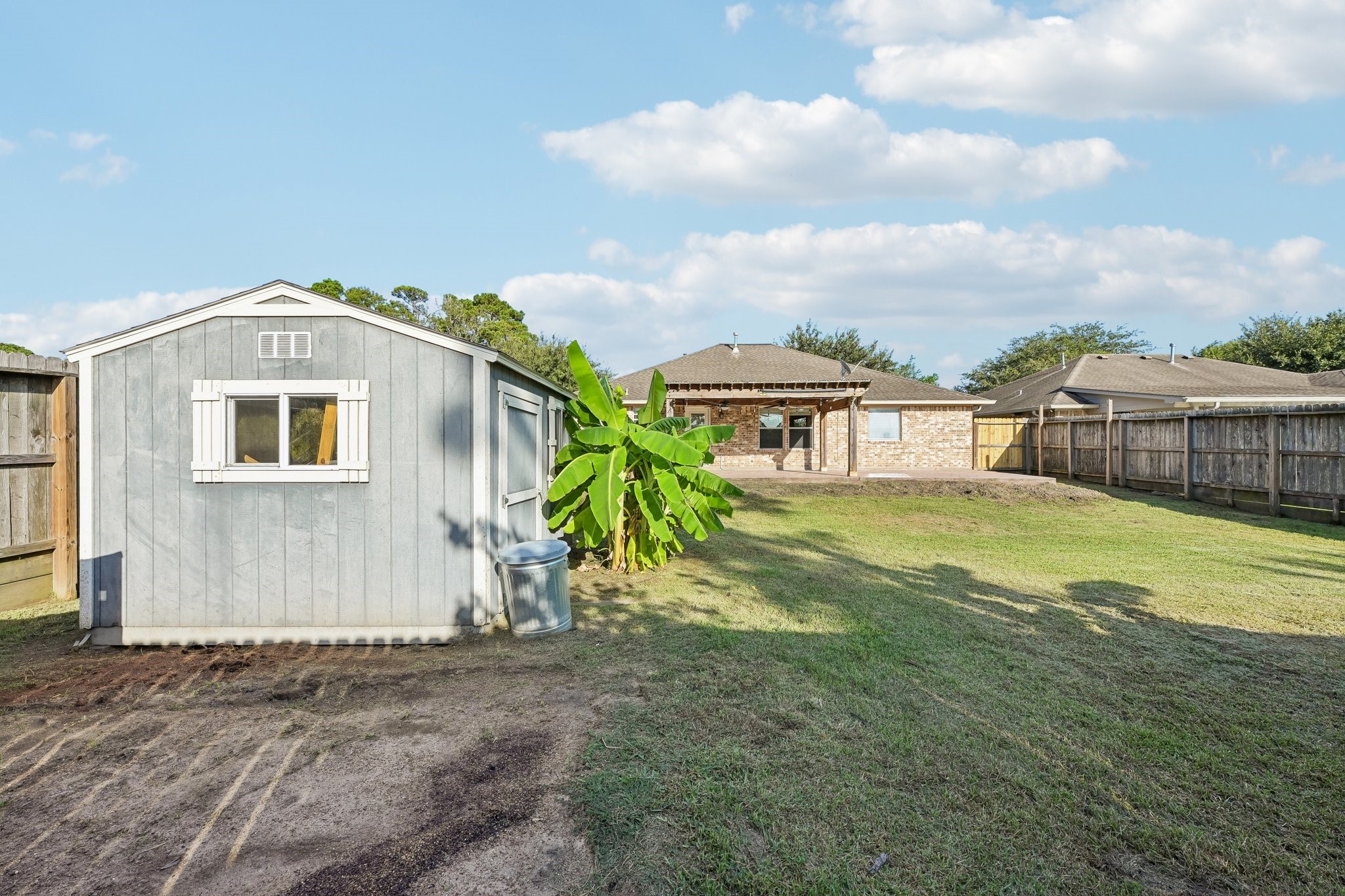 Spacious backyard with a well-maintained lawn, convenient storage shed, and a clear view of the charming brick home, perfect for outdoor activities and relaxation.