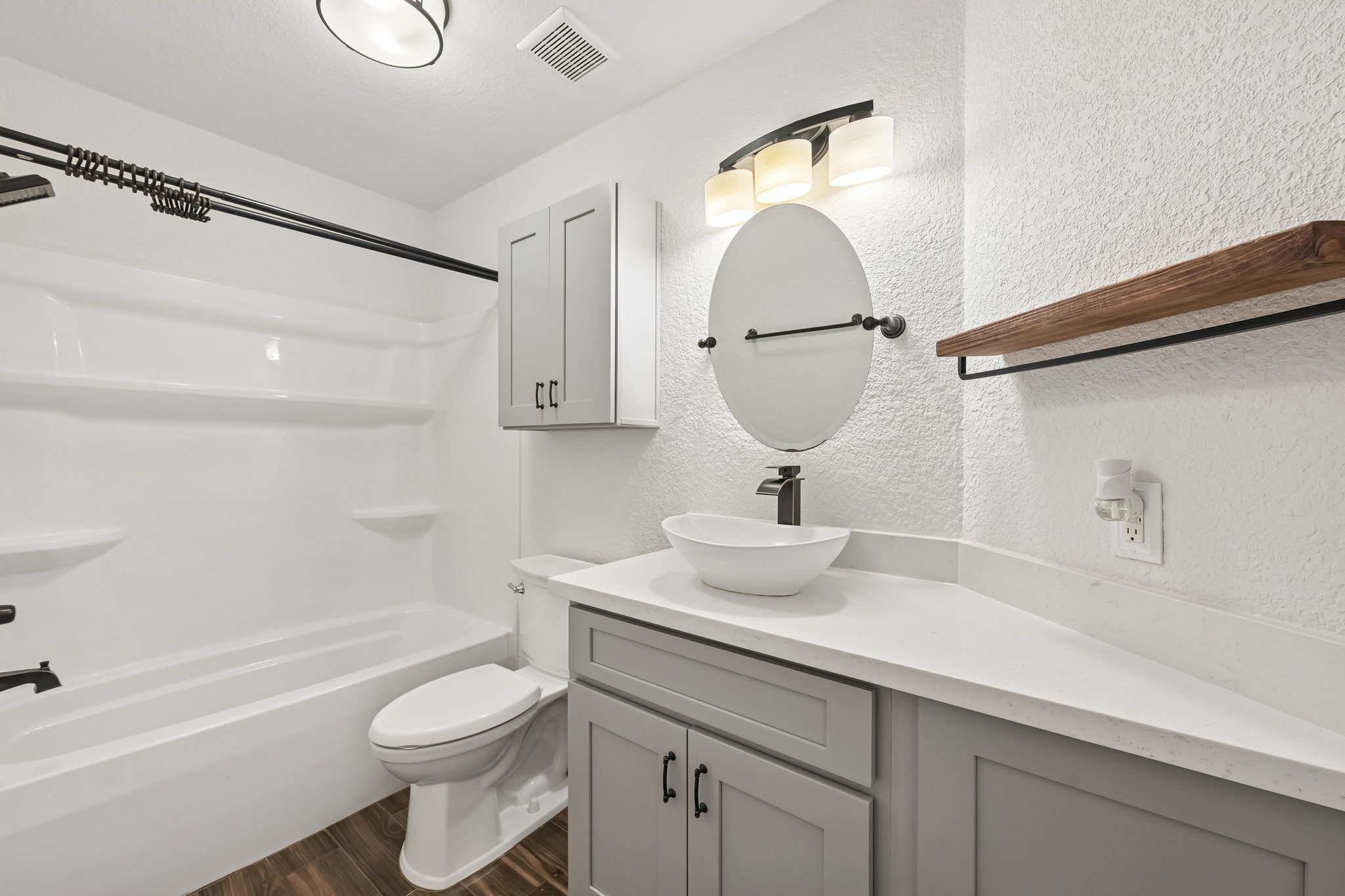 Modern bathroom with elegant fixtures, featuring a sleek vessel sink, stylish round mirror, and a spacious bathtub with built-in shelving.