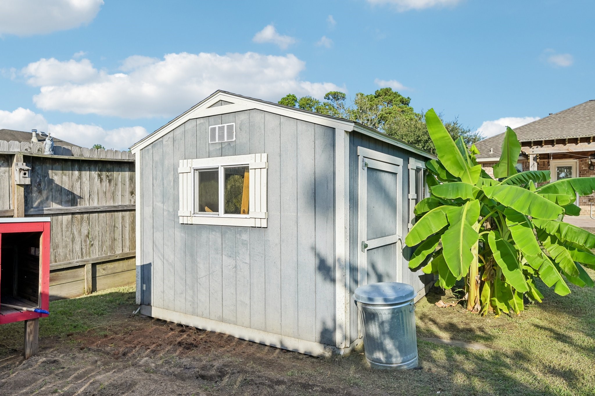 Charming backyard shed with a window, nestled beside lush banana plants, offers convenient storage space in a tranquil setting.