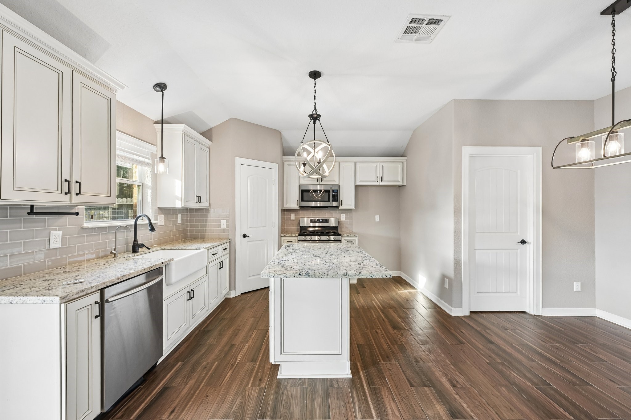 Elegant kitchen with modern stainless steel appliances, granite countertops, and a central island. Features sleek cabinetry, wood-look tile flooring, and stylish pendant lighting for a welcoming atmosphere.