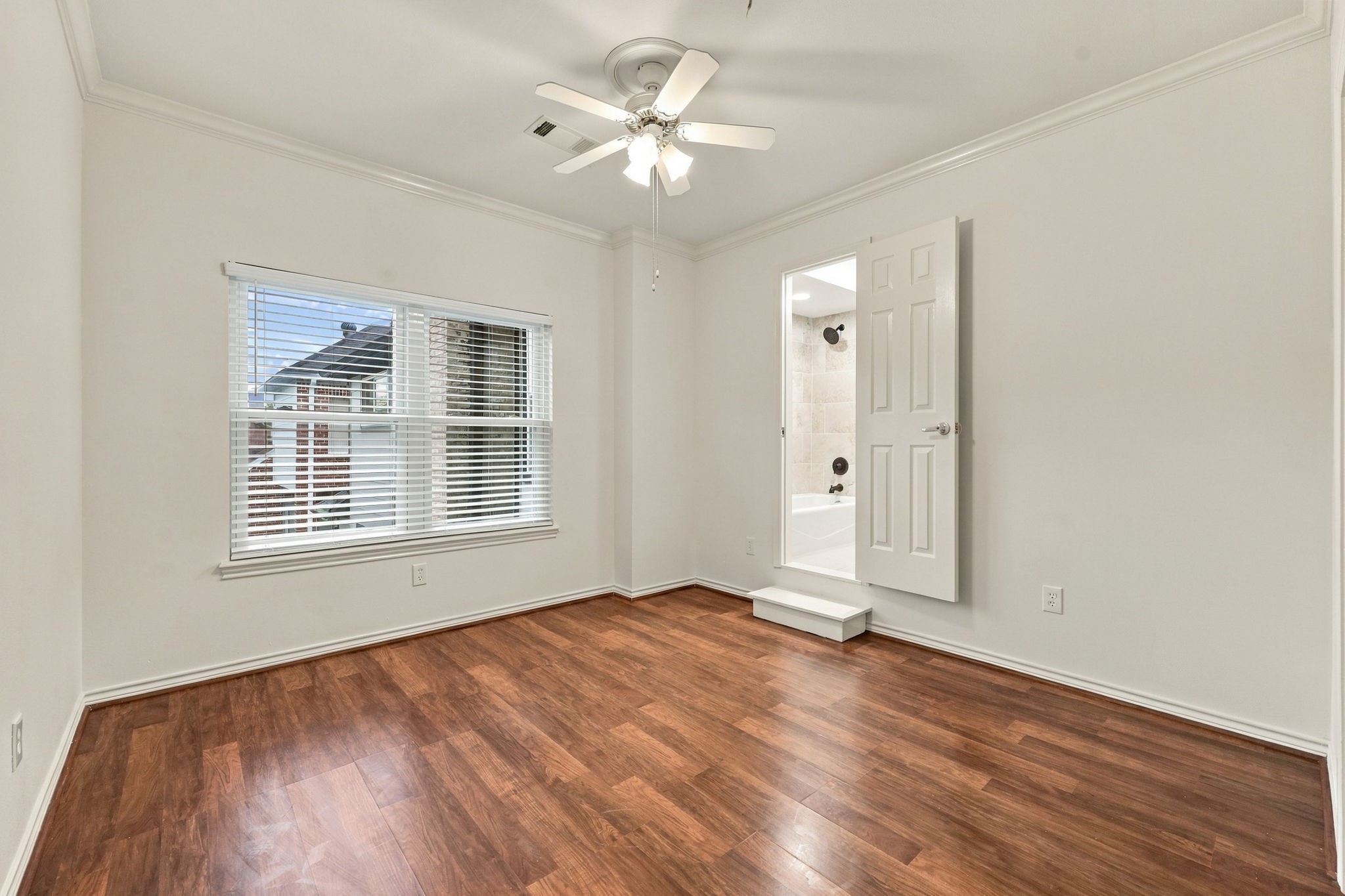 Spacious bedroom with wood-look flooring, ceiling fan, built-in shelving, and multiple windows providing natural light.