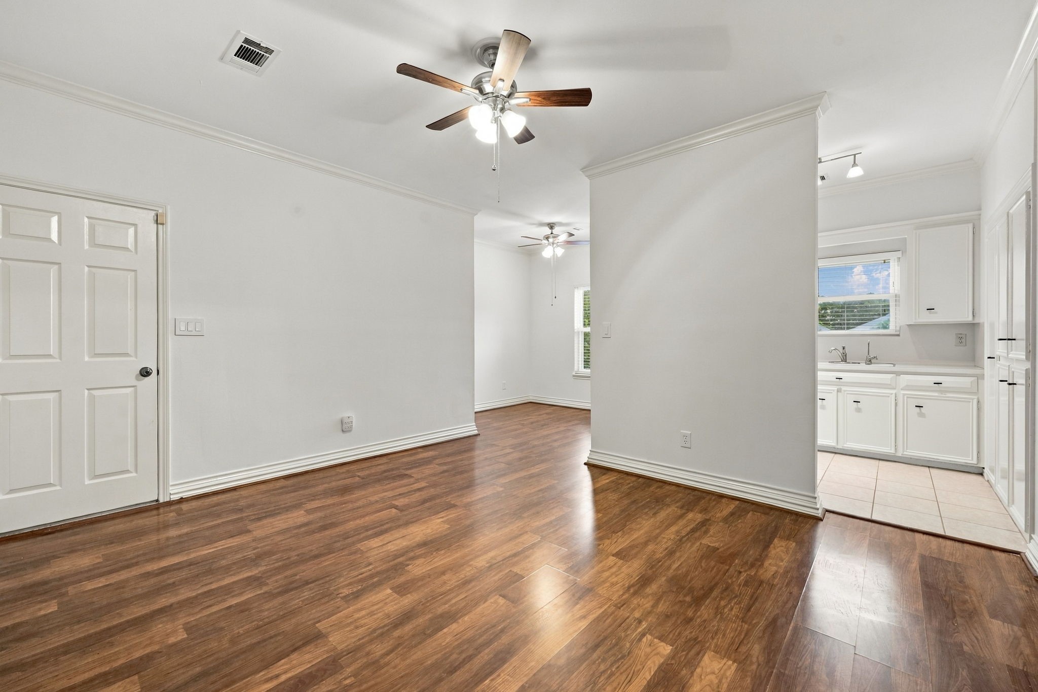 Spacious bedroom with wood-look flooring, ceiling fan, built-in shelving, and multiple windows providing natural light.