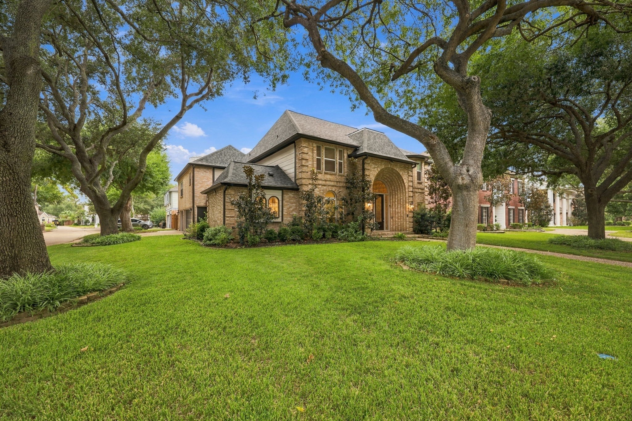Impressive two-story brick residence situated on a corner lot, showcasing mature trees, manicured landscaping, and a welcoming entry.