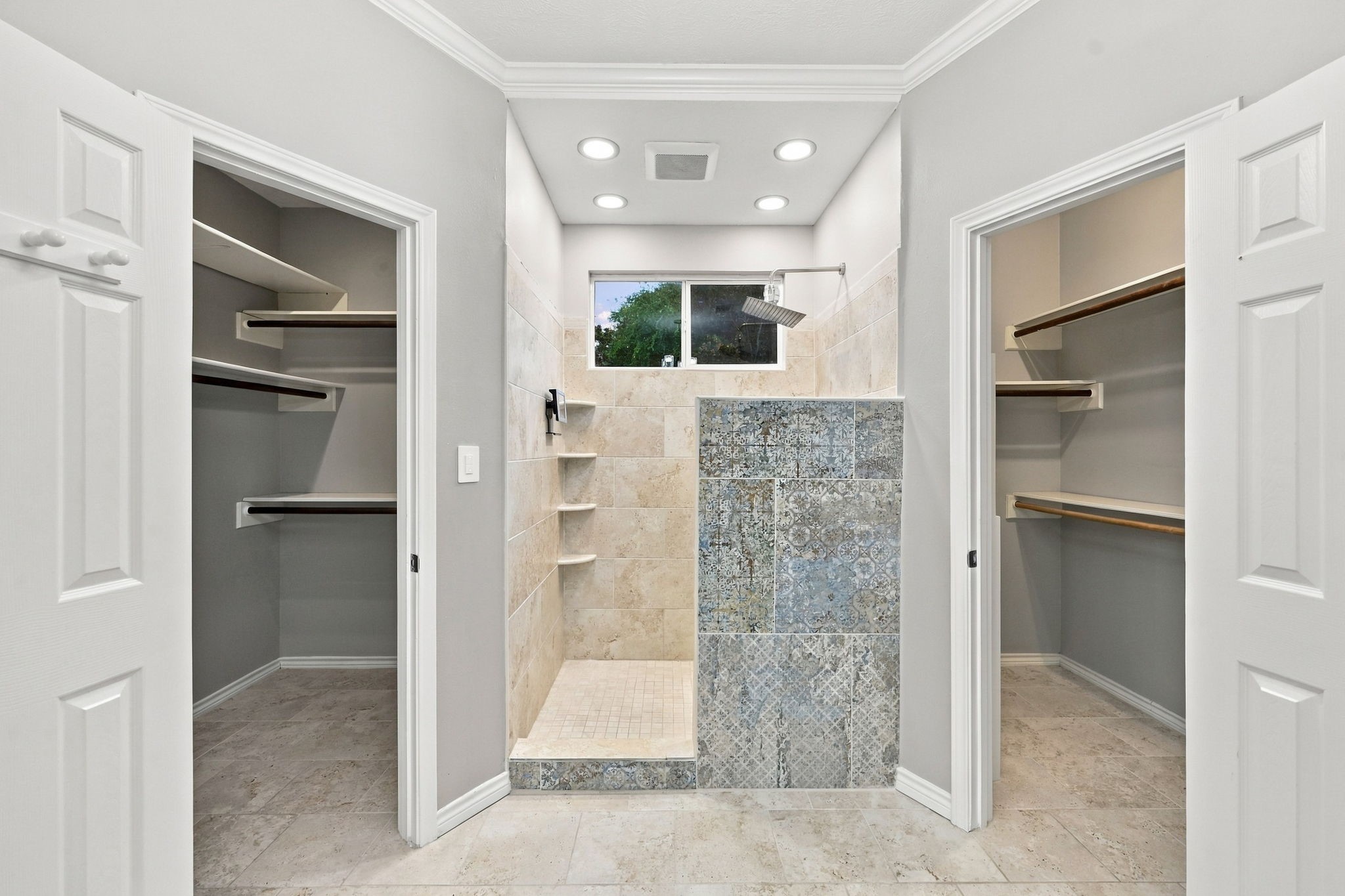 Spacious walk-in shower with decorative tile detailing, built-in shelving, and modern fixtures.