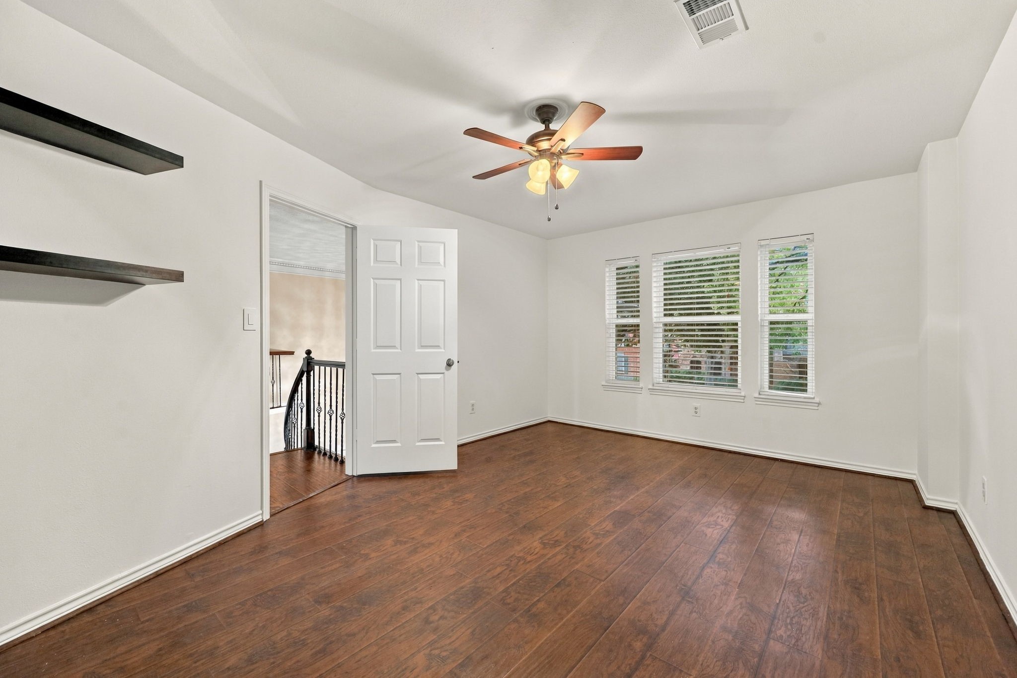 Bright bedroom featuring wood-look flooring, multiple windows, a ceiling fan, and access to the upper-level landing.