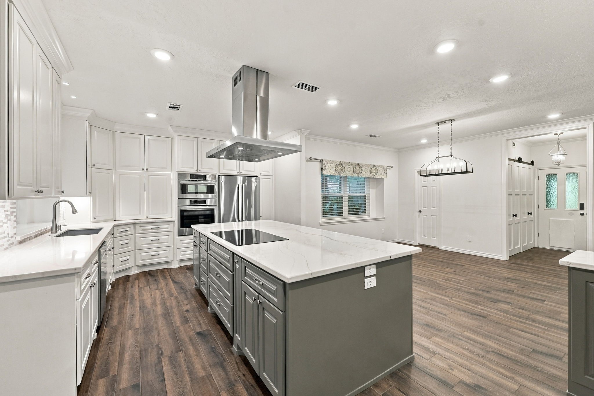 Updated kitchen featuring a large gray island, white cabinetry, stainless steel appliances, and contemporary lighting.