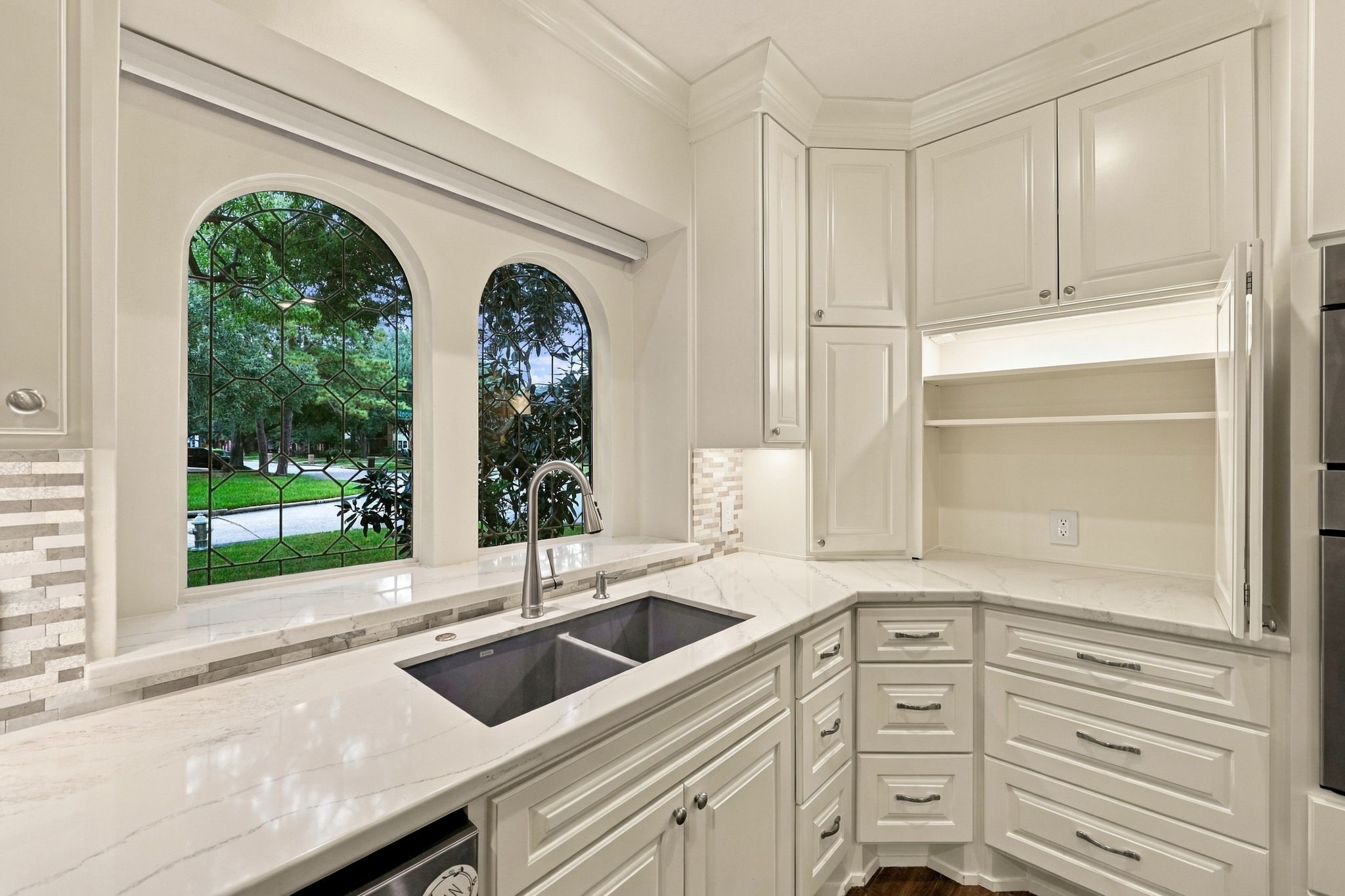 Kitchen sink positioned beneath elegant arched windows, complemented by white cabinetry and stone countertops.