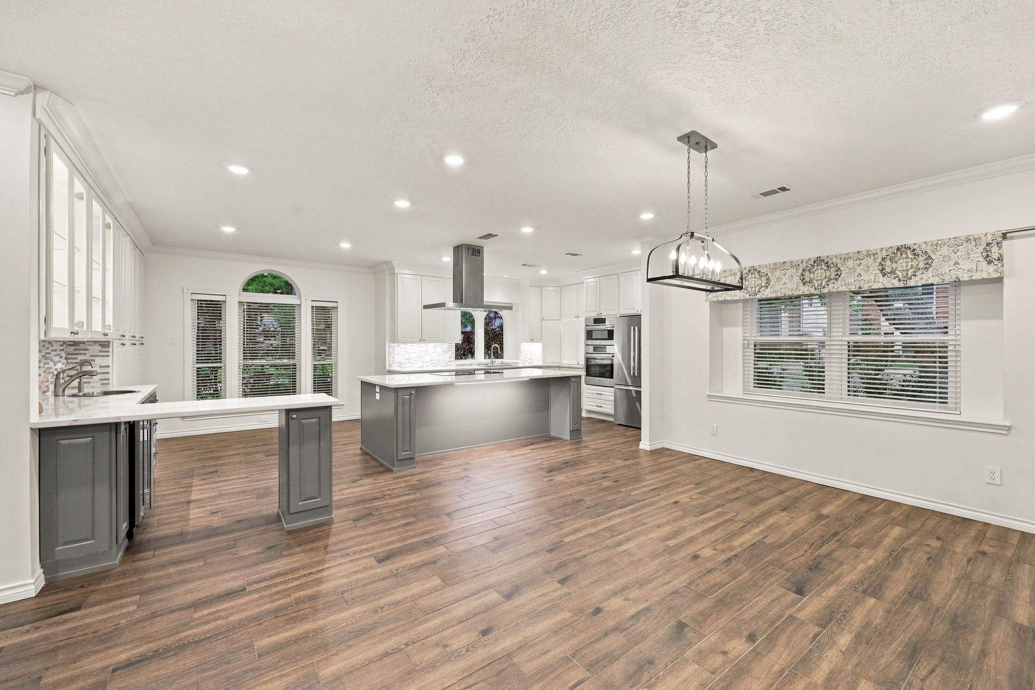 Open-concept kitchen and dining space featuring white cabinetry, a gray island, modern finishes, and wood-look flooring.