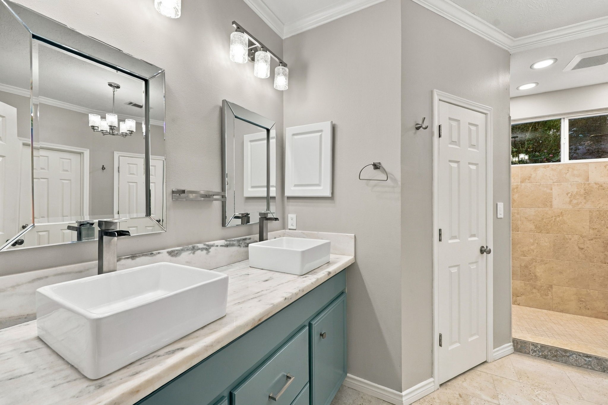 Contemporary bathroom with dual vessel sinks, a teal vanity, elegant mirrors, and a spacious walk-in shower.