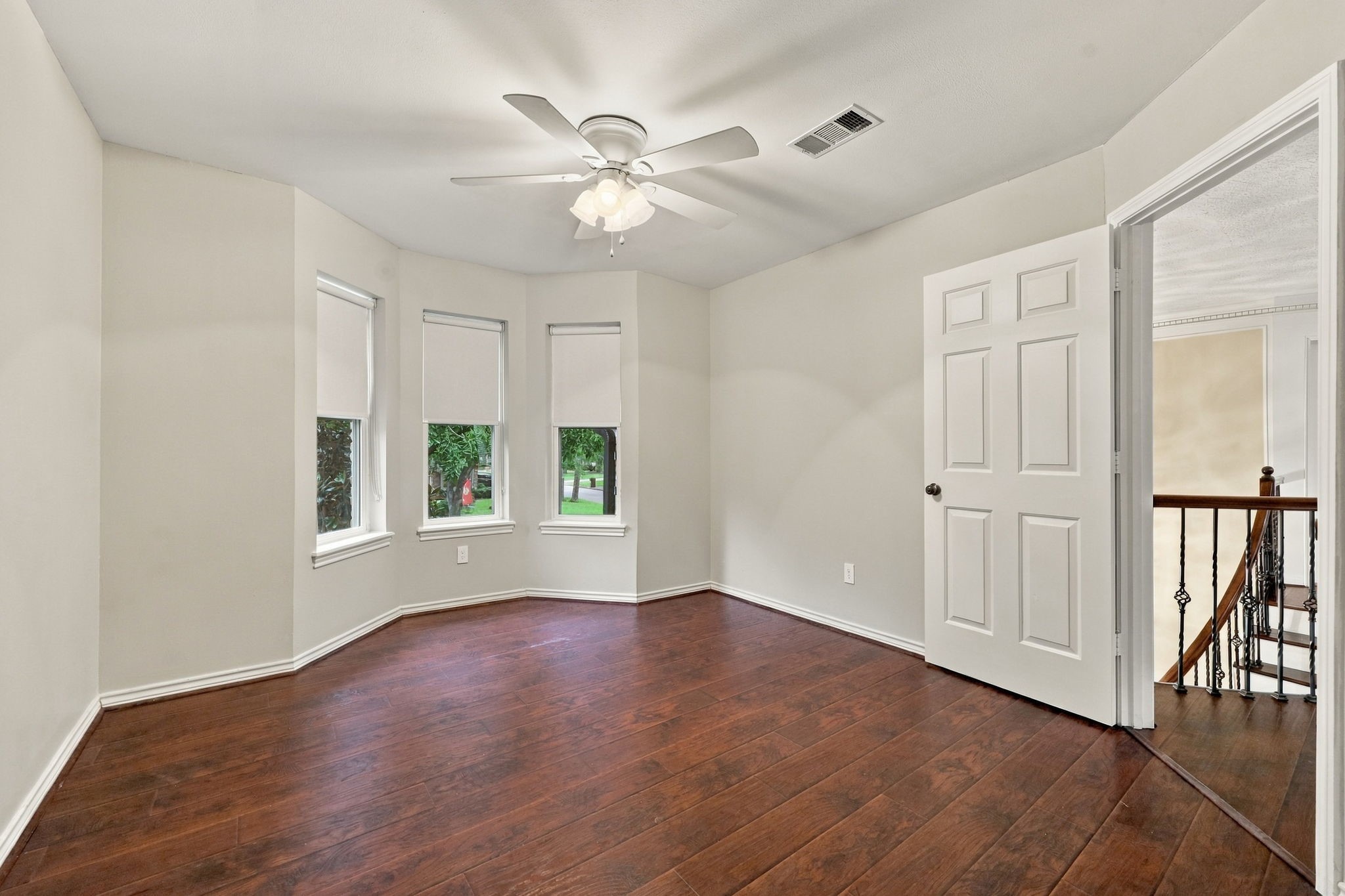 Bright bedroom featuring wood-look flooring, multiple windows, a ceiling fan, and access to the upper-level landing.