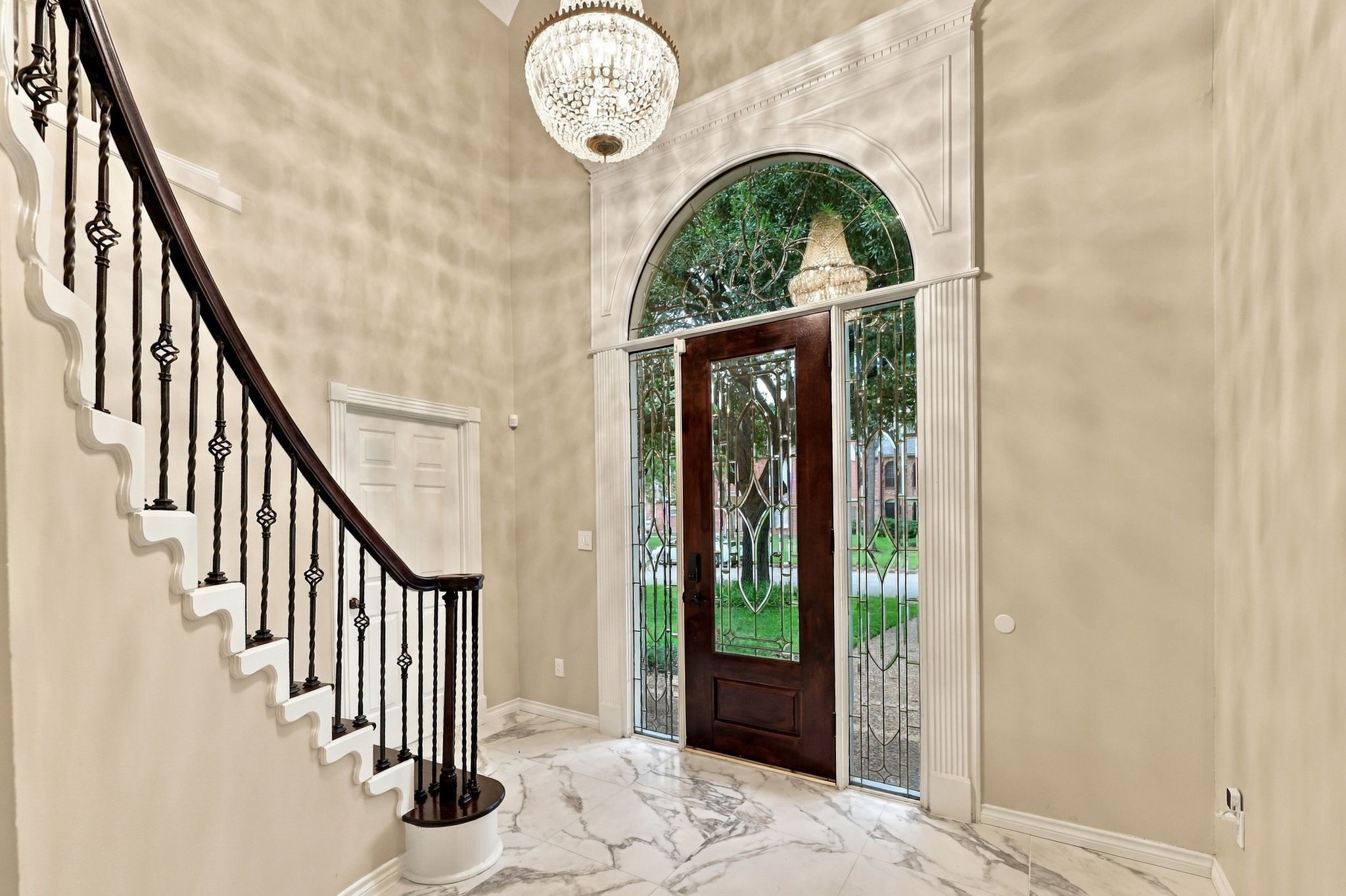 Grand entry foyer featuring marble-look flooring, a decorative chandelier, and a sweeping staircase with dark wood railings.