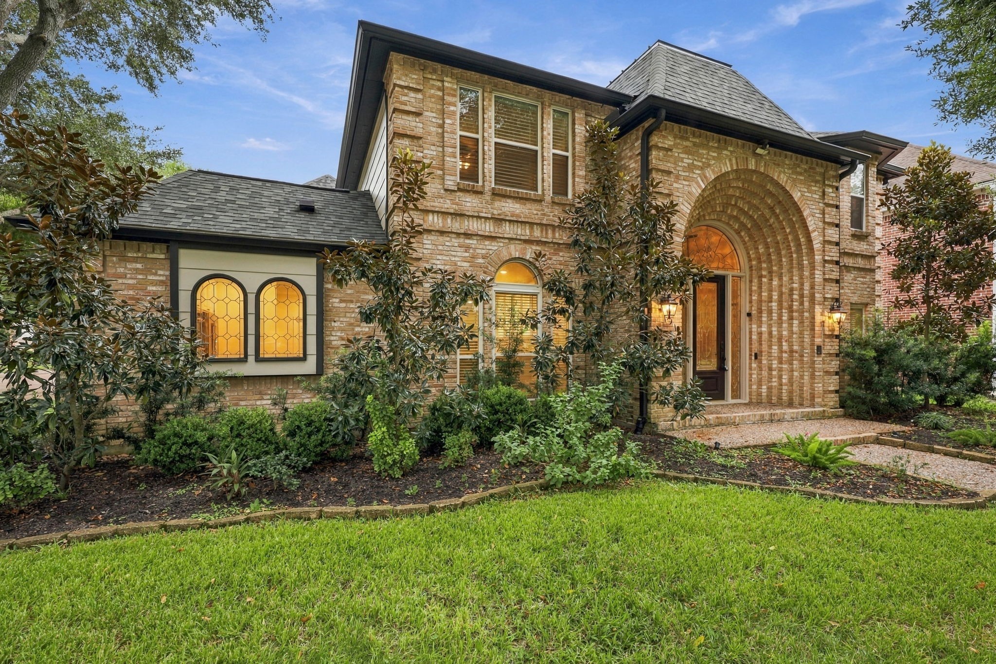 Beautiful brick home featuring mature shade trees, lush landscaping, and an inviting front lawn.