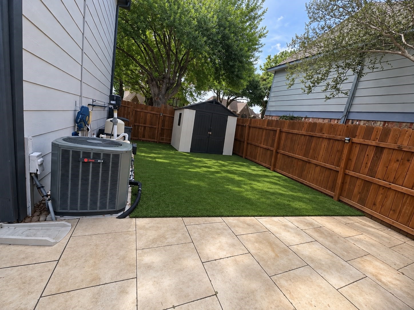 Fenced side yard with green space and a paved patio area, offering additional outdoor utility and room for storage.