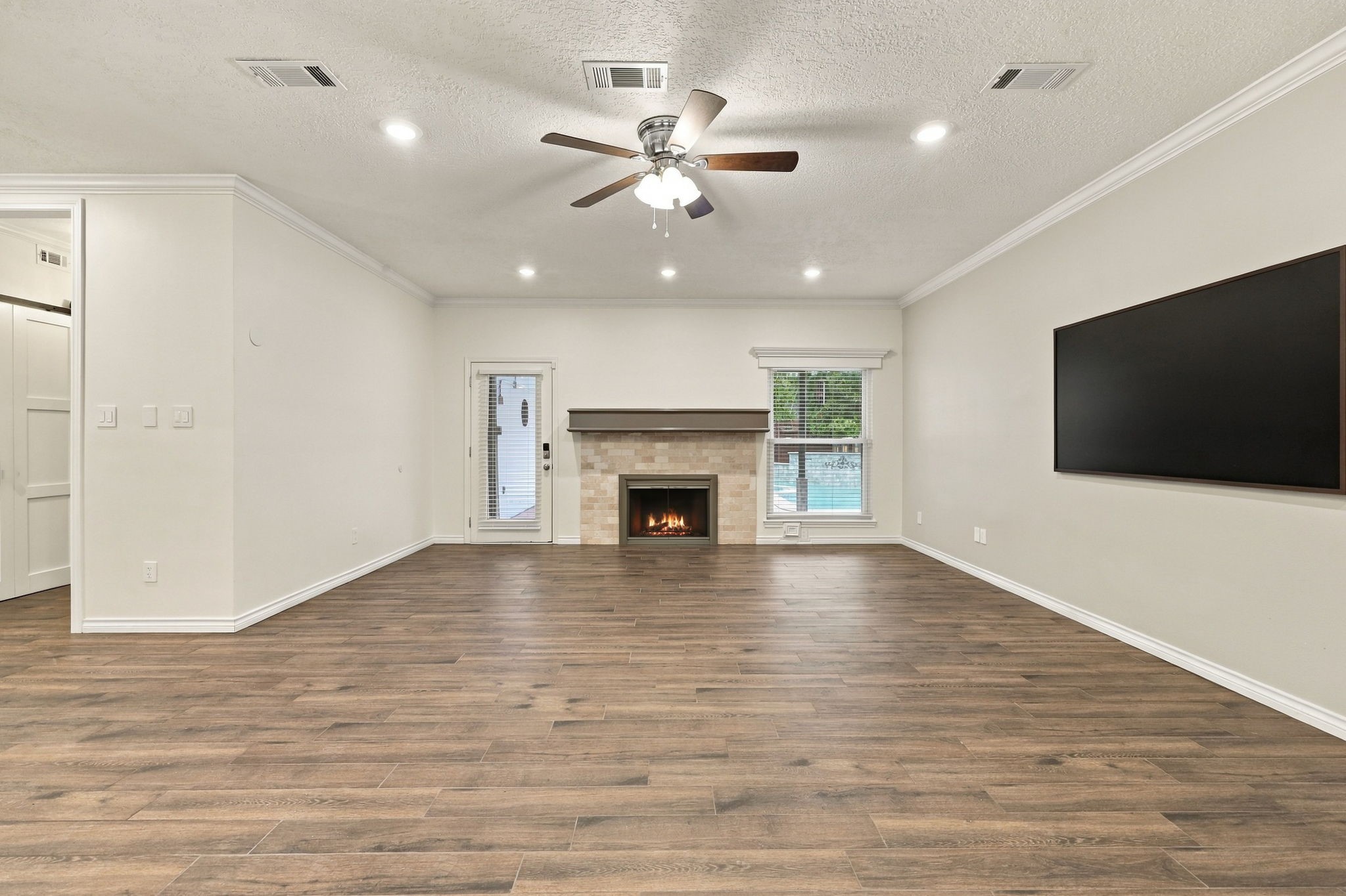 Spacious living room with wood-look flooring, recessed lighting, a fireplace, and a large wall-mounted TV.