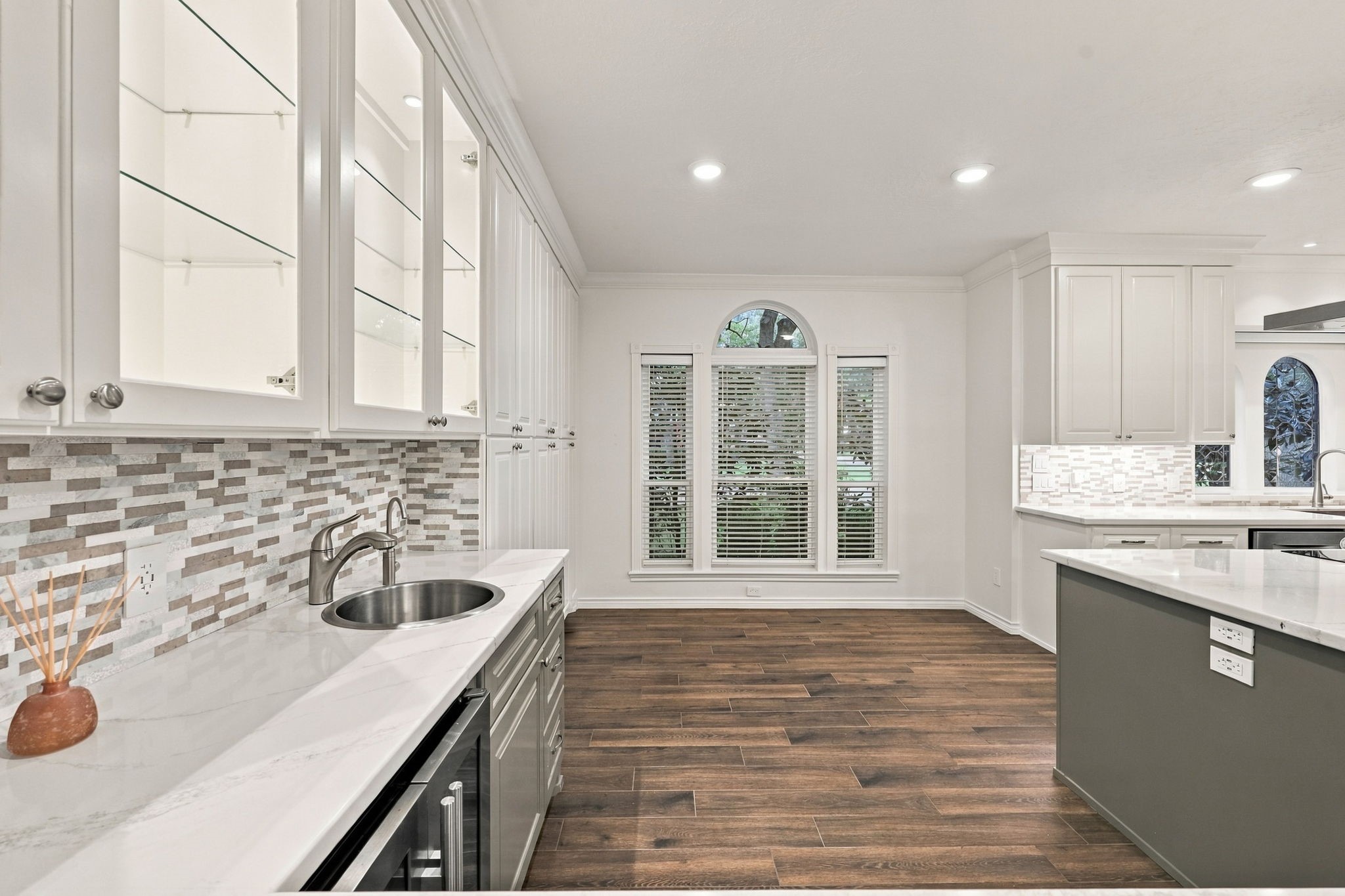 Kitchen sink positioned beneath elegant arched windows, complemented by white cabinetry and stone countertops.