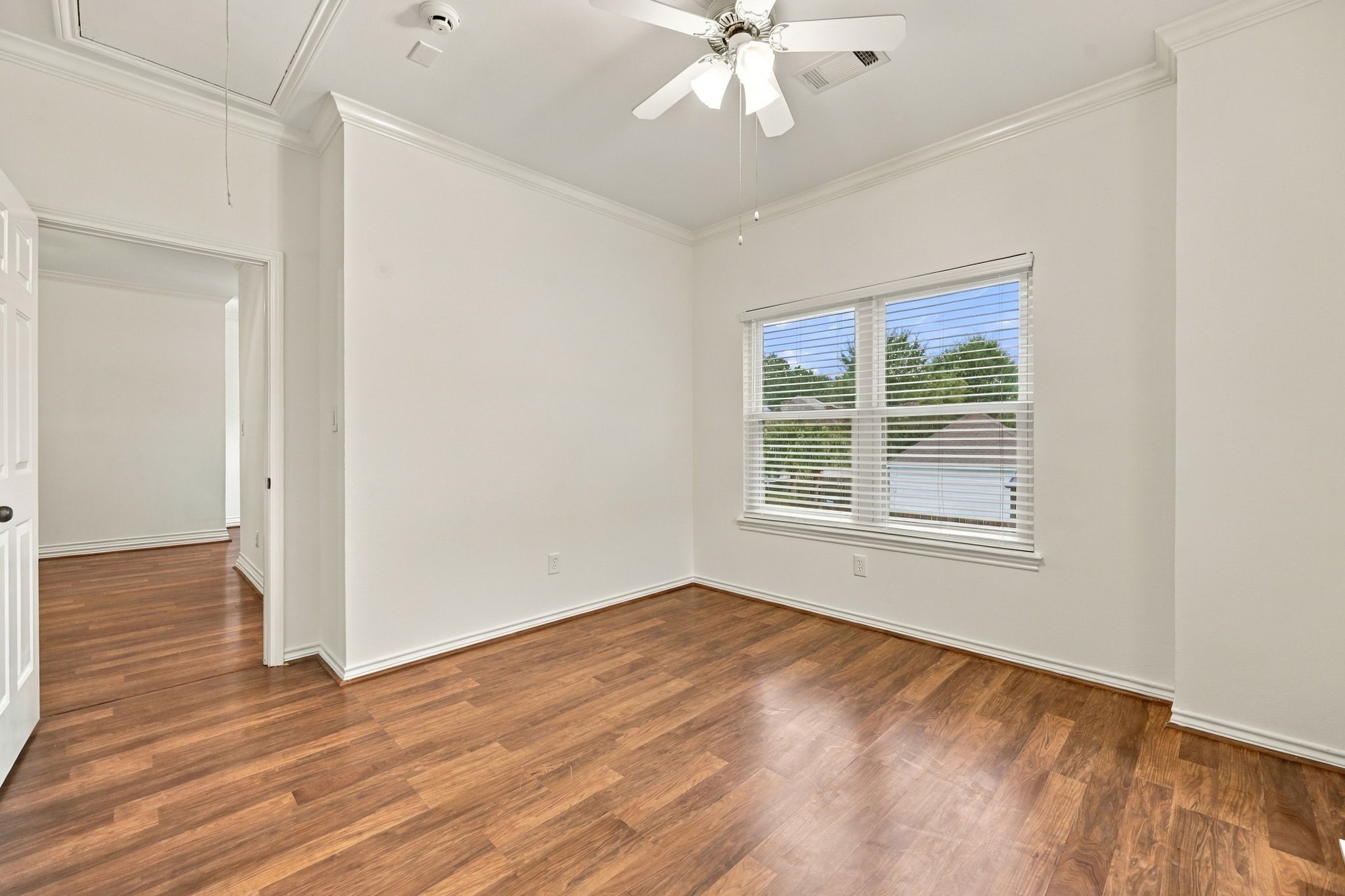 Spacious bedroom with wood-look flooring, ceiling fan, built-in shelving, and multiple windows providing natural light.