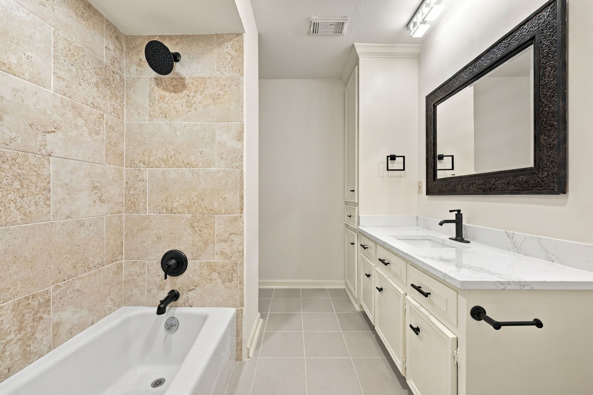 Bathroom featuring a modern vanity, decorative mirror, and a tub/shower combination with tile surround.