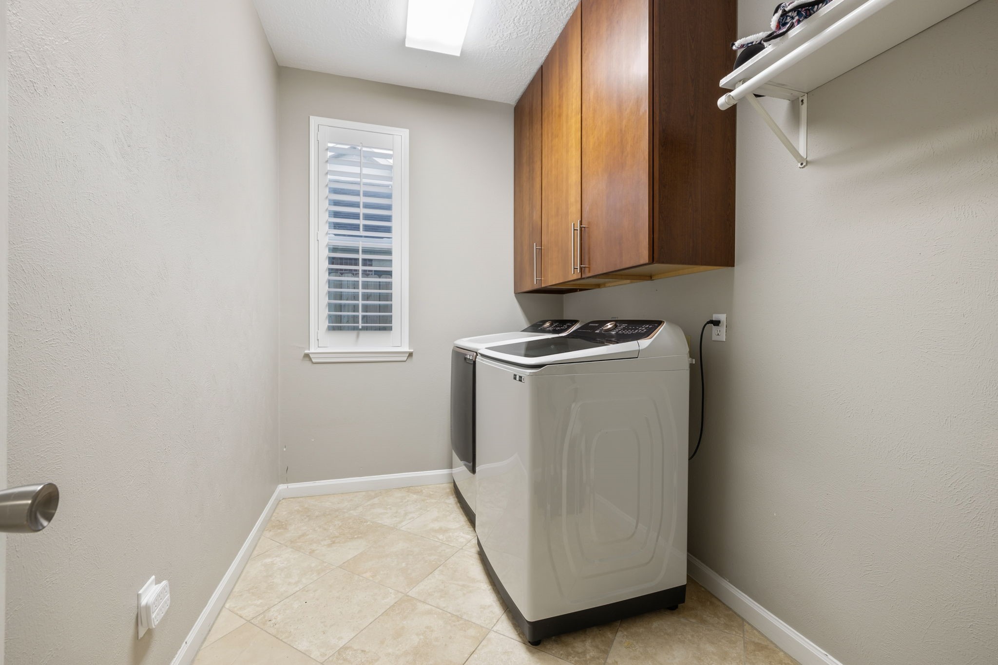 Modern laundry room featuring a sleek washer and dryer, ample cabinet storage, and a bright window with shutters.