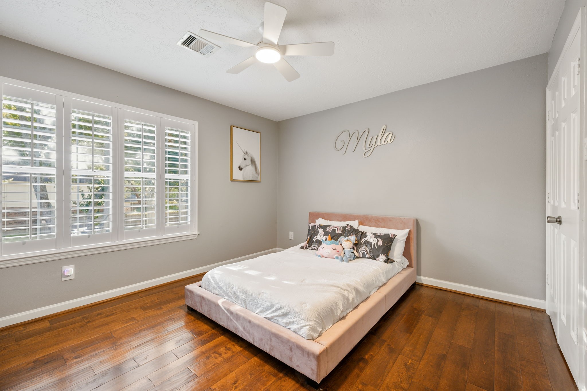 Bright and inviting bedroom featuring hardwood flooring, plantation shutters, and a contemporary ceiling fan