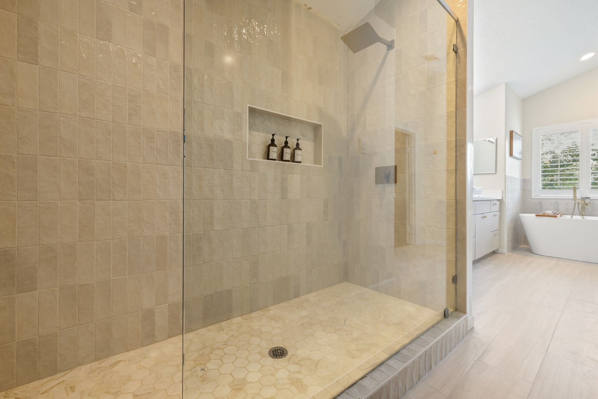 Oversized walk-in shower with floor-to-ceiling tile, glass enclosure, rainfall showerhead, and recessed storage niche.  There is also built-in cabinets directly across from the shower for additional linen storage.