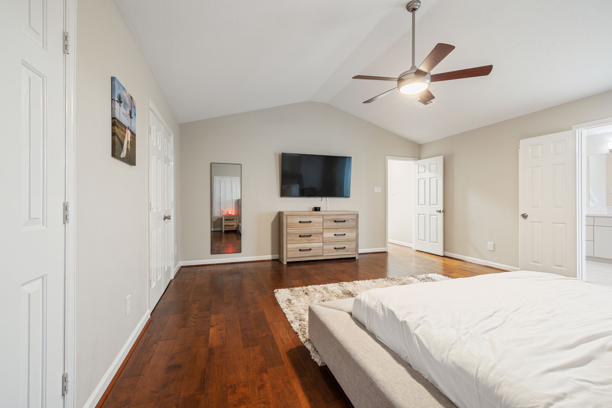 Spacious bedroom featuring hardwood floors, a modern ceiling fan, and ample natural light, complemented by a sleek dresser and wall-mounted TV.