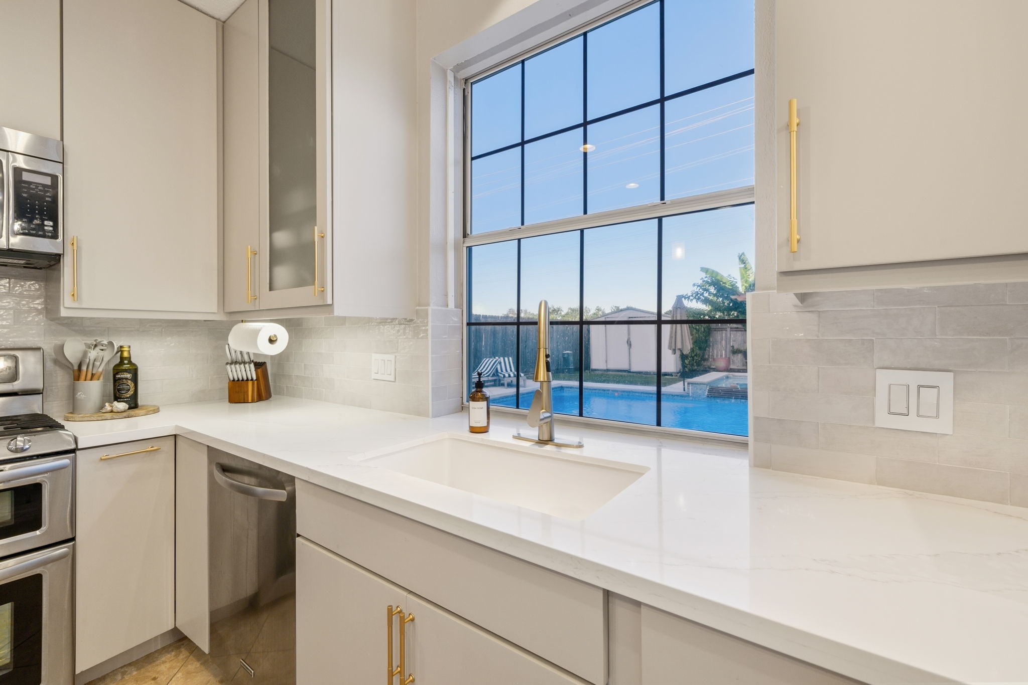 A picturesque pool view framed by a striking window above the kitchen sink.