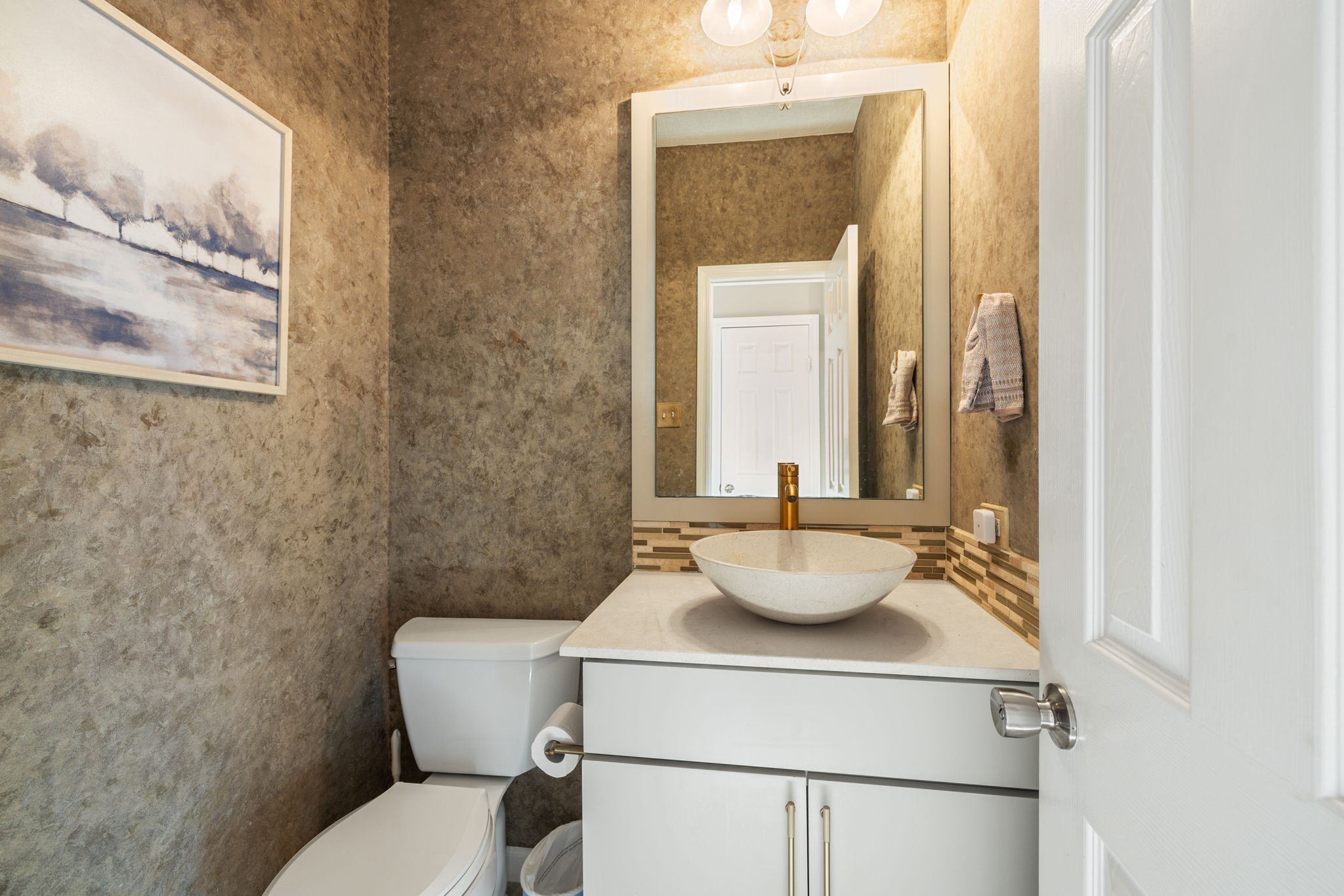 Stylish first-floor powder room with a contemporary vessel sink, decorative tile accents, and warm textured walls.