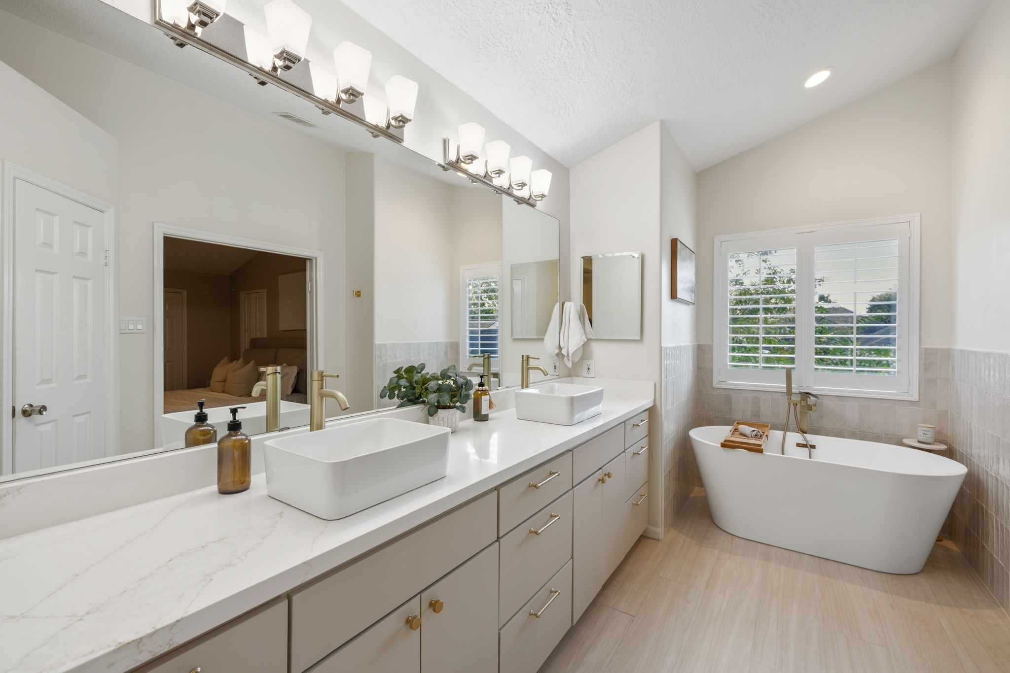 Beautifully updated primary bath featuring dual vessel sinks, a freestanding soaking tub, and sophisticated gold-tone fixtures.