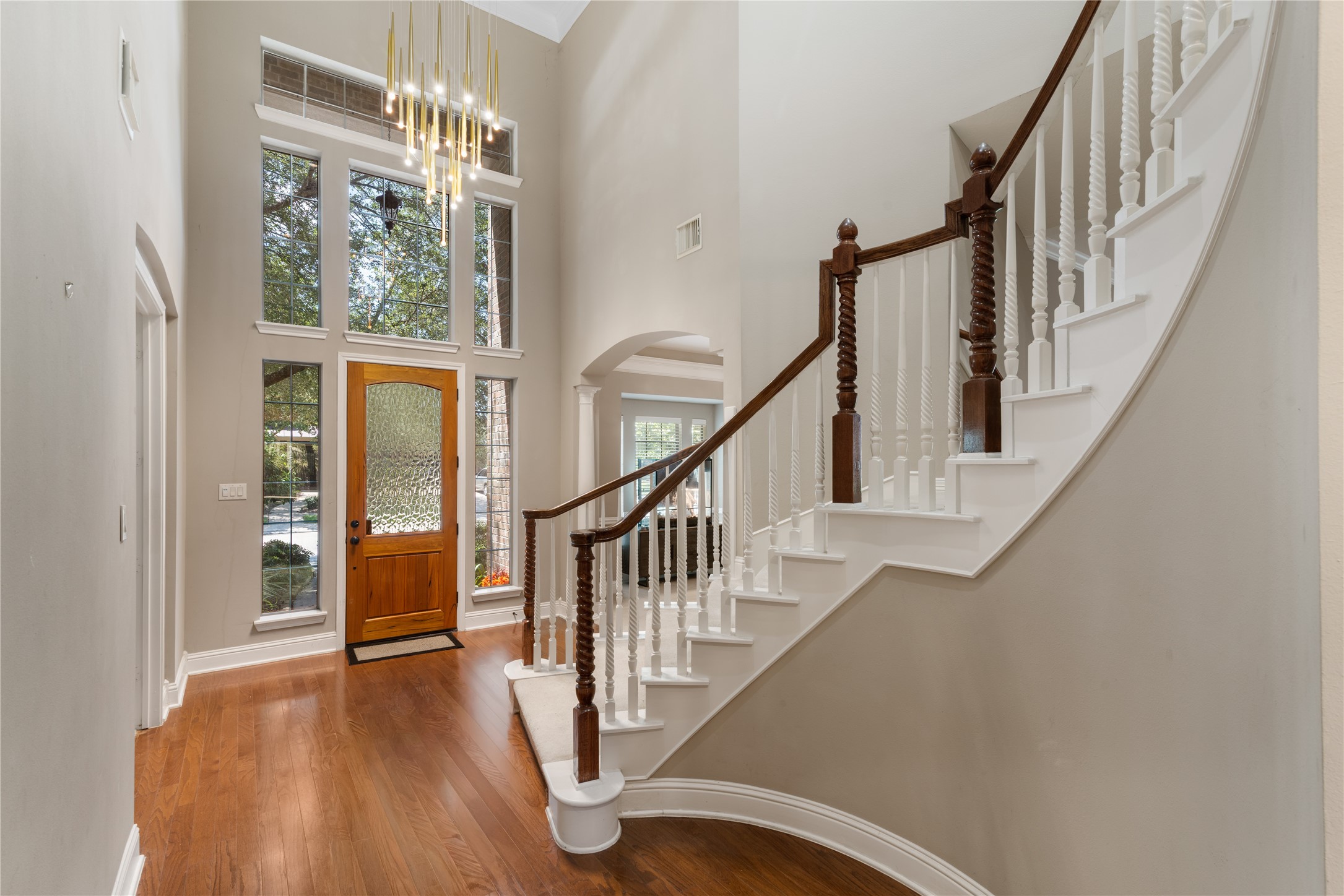 Stunning foyer with soaring ceilings, wood front door with decorative glass, tall surrounding windows fills the space with natural light, and a modern chandelier adds a luxurious touch.