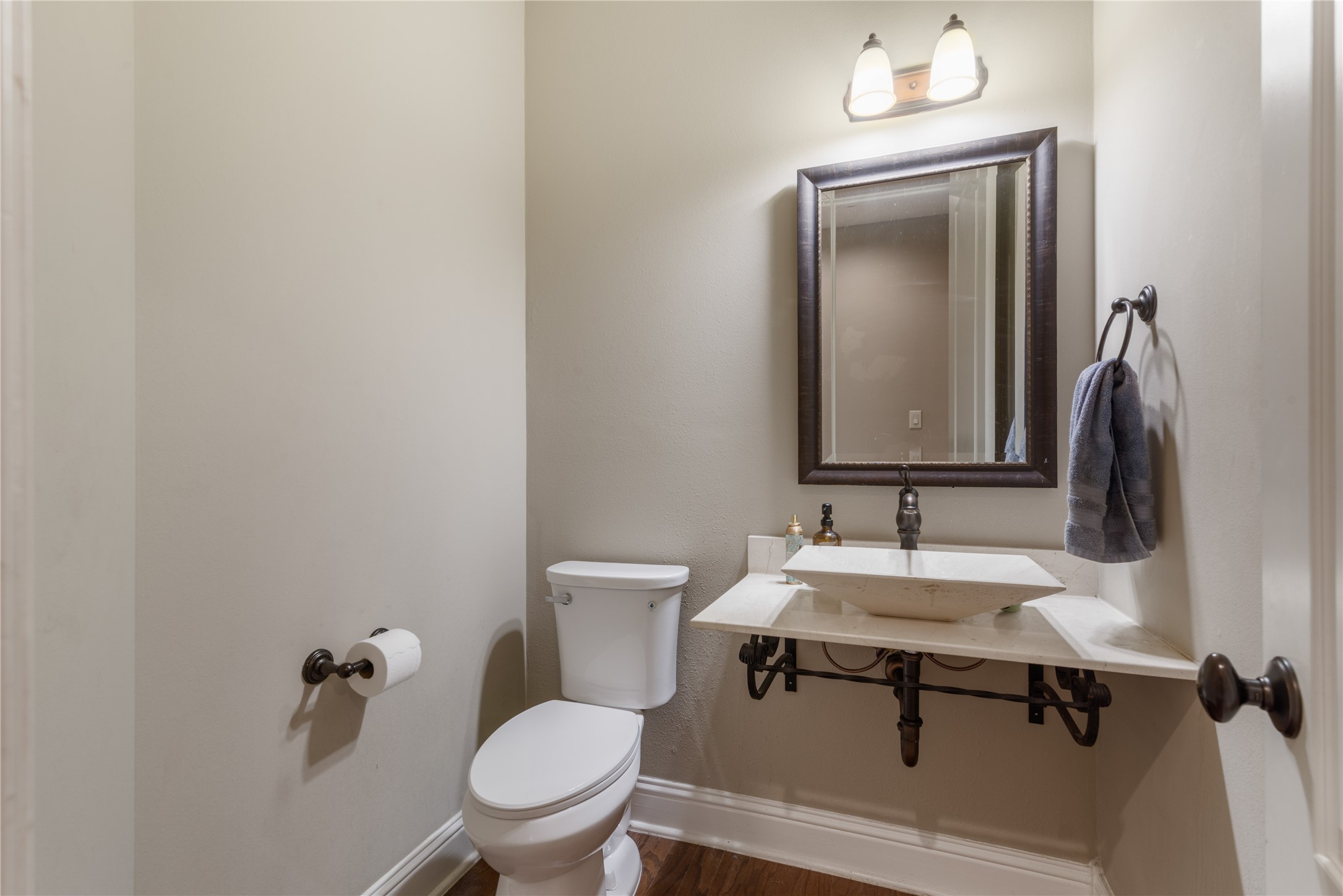 Stylish half bath featuring a modern vessel sink, warm toned floors and neutral tones creating an updated space perfect for guests.