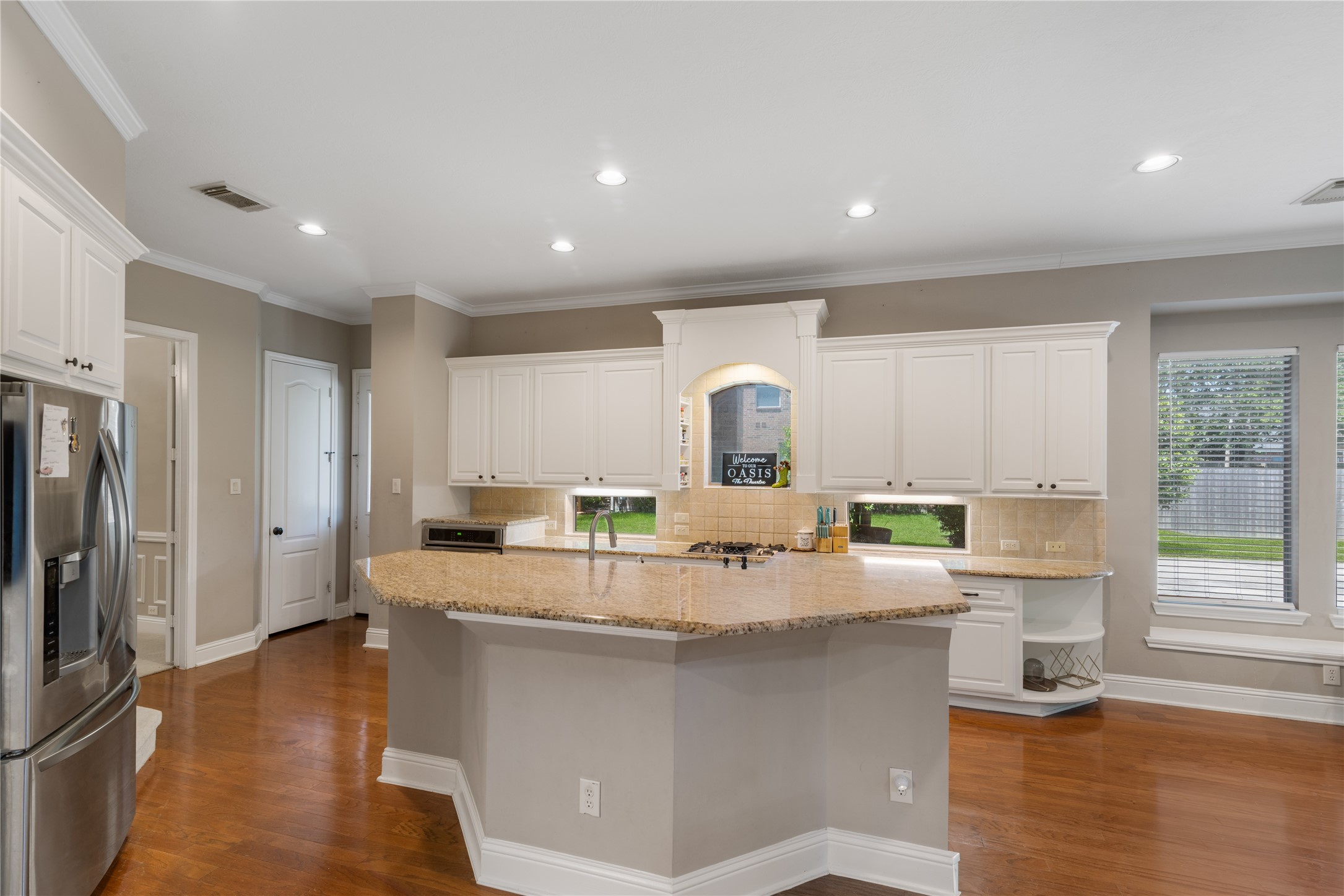 The large island offers excellent workspace and seating, while recessed lighting and big windows fill the space with natural light.