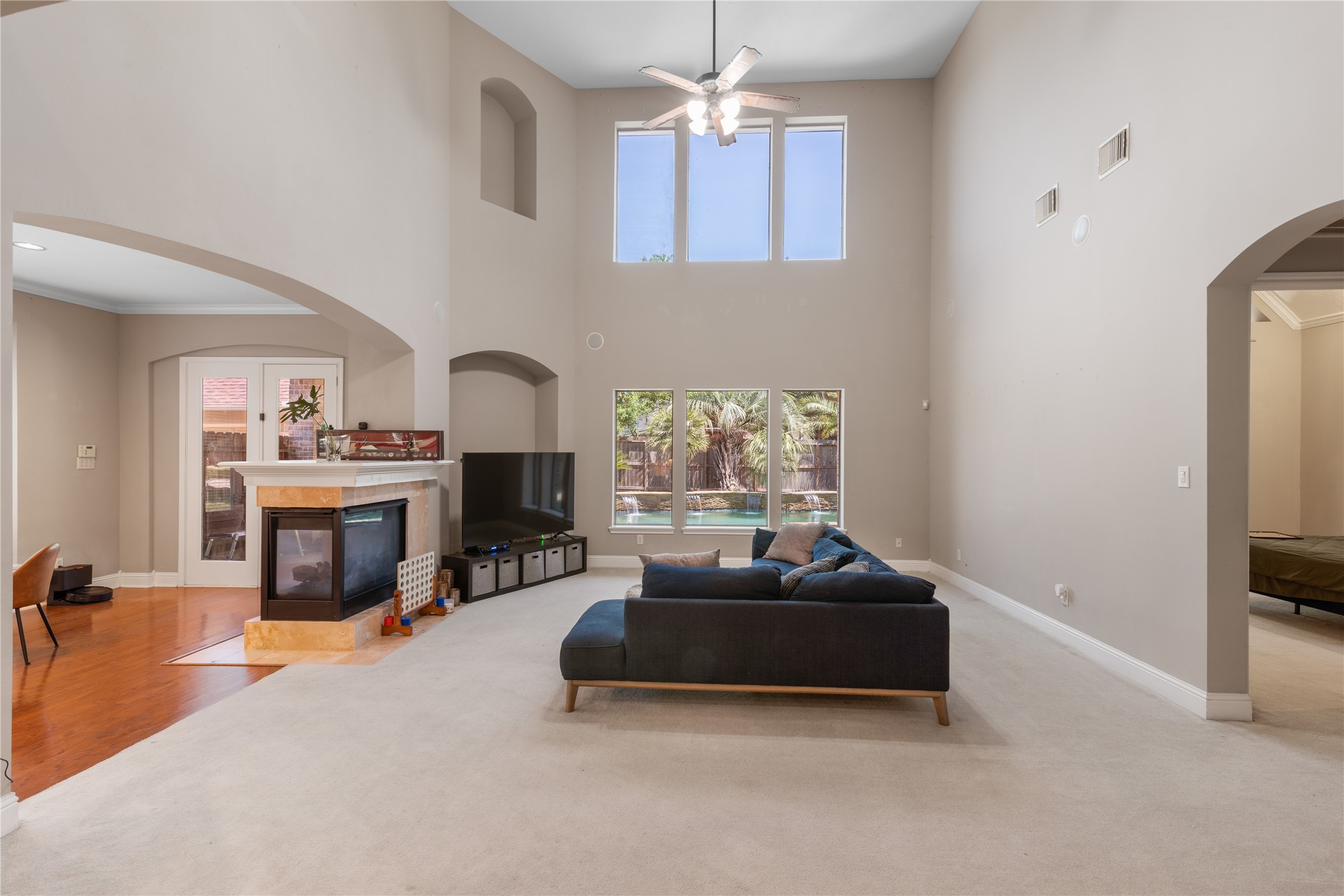 Light-filled family room with high ceilings, double-sided fireplace, and views of the pool area.