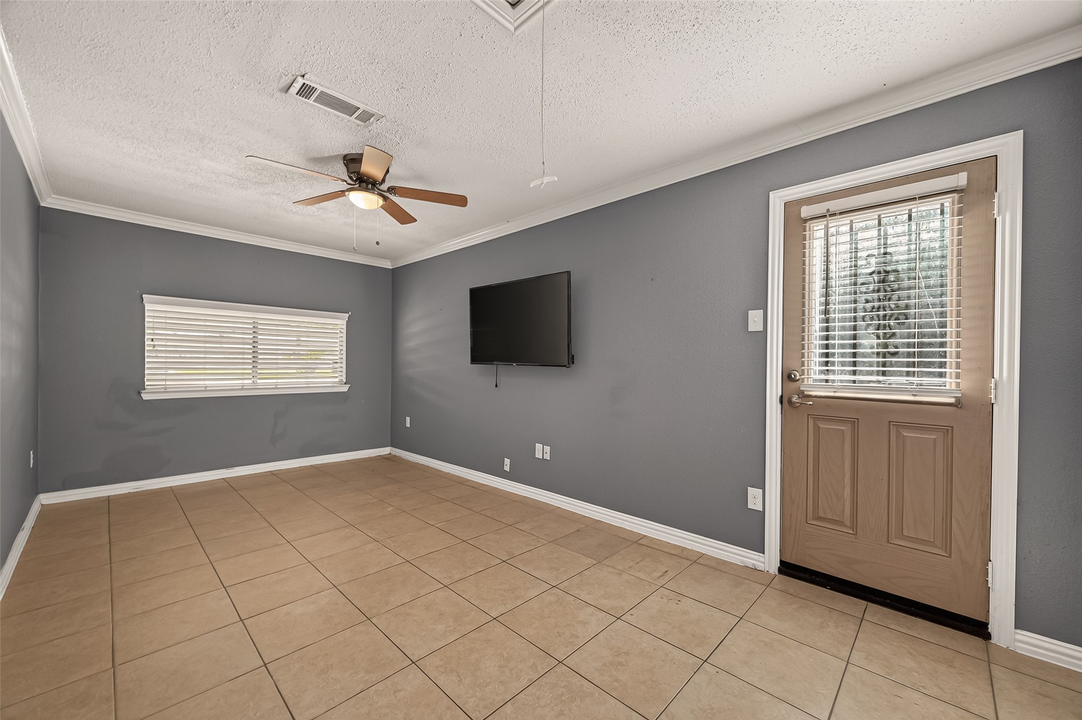 Flexible living area with tile flooring, crown molding, ceiling fan, and French doors. Perfect as a home office, den, game room, or hobby space.