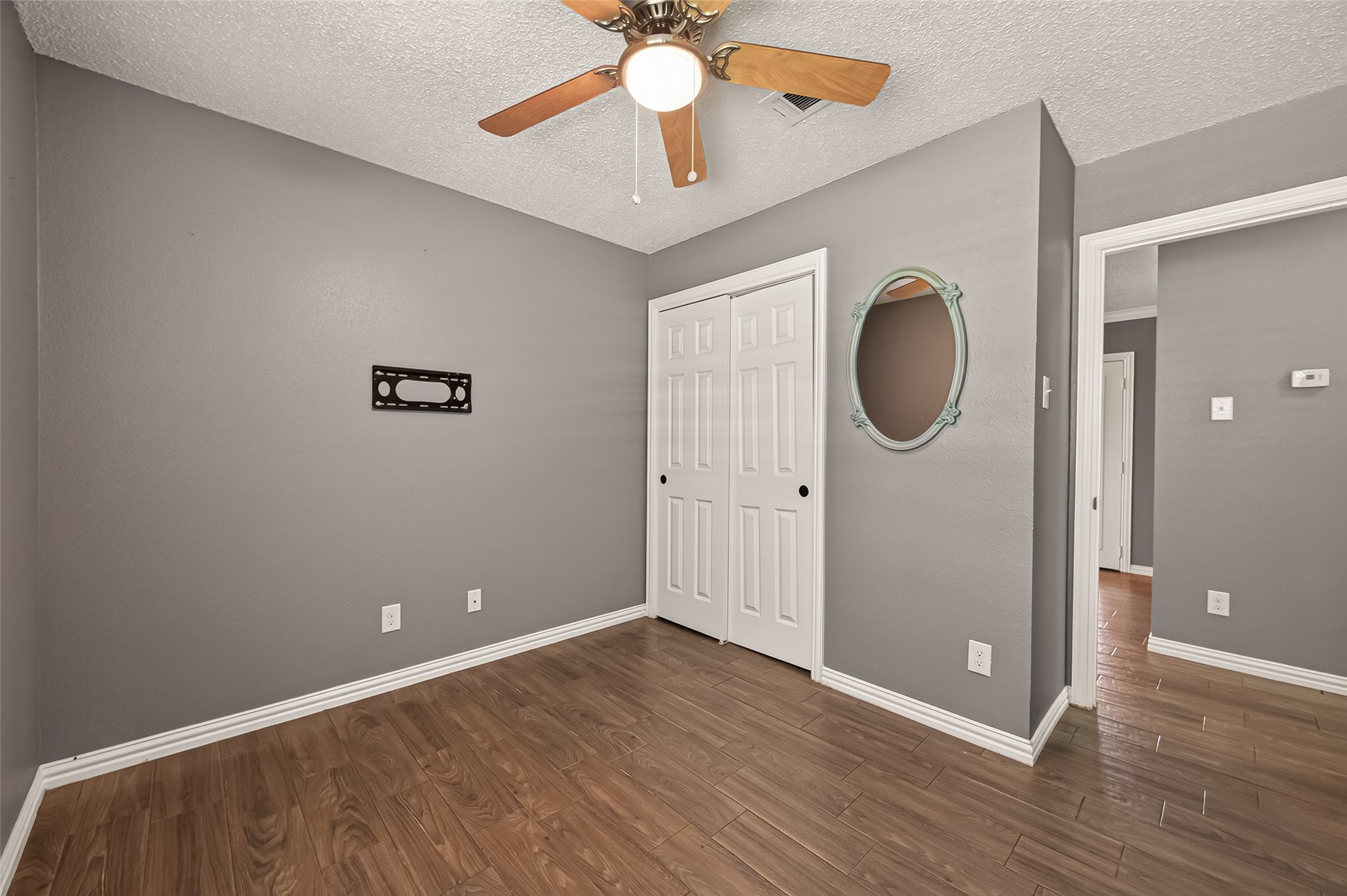 Inviting secondary bedroom featuring durable wood-look tile flooring, neutral paint, a ceiling fan with light, and a spacious closet with sliding doors. A versatile space ideal for a bedroom, home office, or guest room.