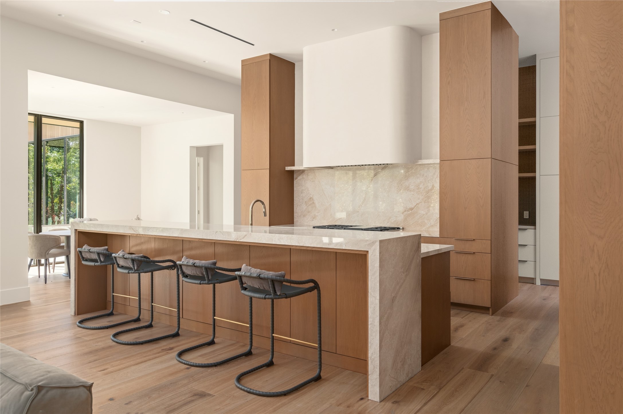 The centerpiece of the chef's kitchen is a striking 13-foot waterfall island finished in Daino Reale marble, offering generous seating and preparation space while complementing the warmth of the custom white oak cabinetry.