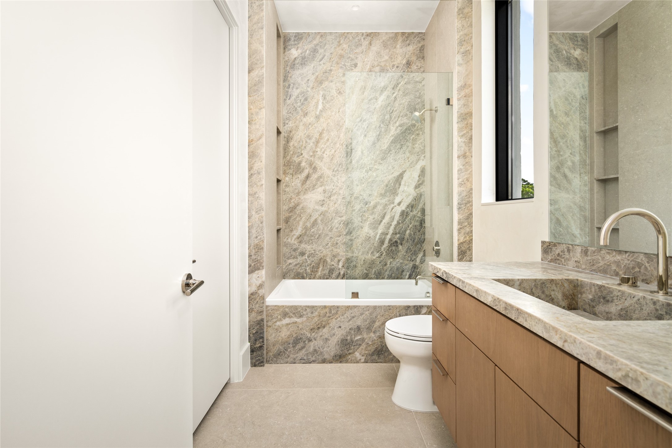 The ensuite bathroom showcases a Cielo quartzite vanity with an integrated sink and elegant Luxe Stone Chablis flooring, and a custom backlit mirror. Sophisticated finishes and clean lines create a sleek, contemporary space.