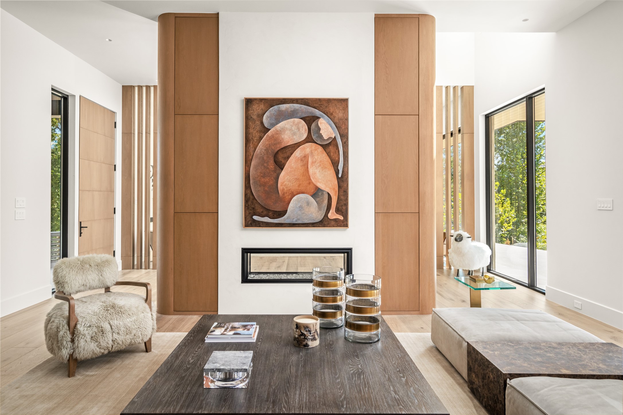 A closer look at the family room reveals the beautiful symmetry of the double-sided fireplace, framed by softly curved white oak millwork, with architectural openings on either side that offer glimpses into the adjoining spaces.