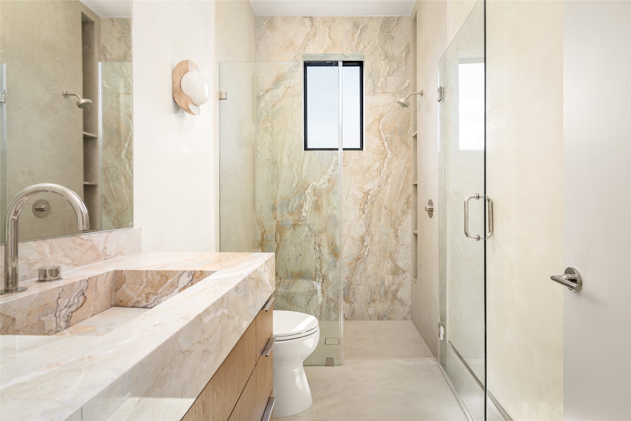 A sleek floating vanity topped with Dolce Vita quartzite and an integrated sink adds a luxurious touch to this ensuite bathroom, while Luxe Stone Montpellier wall and floor tile beautifully complements the spacious glass-enclosed shower.
