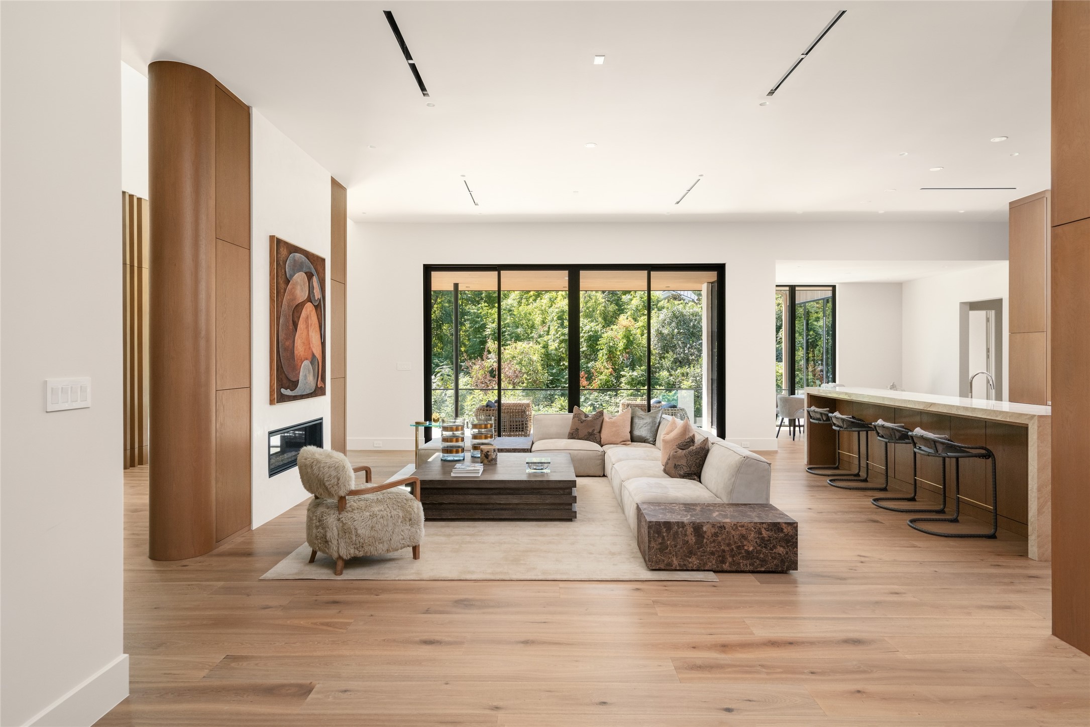 A beautifully composed living space where the family room and kitchen come together, with warm wood finishes, thoughtfully curated architectural details, and expansive glass creating an inviting setting for both relaxing and entertaining.