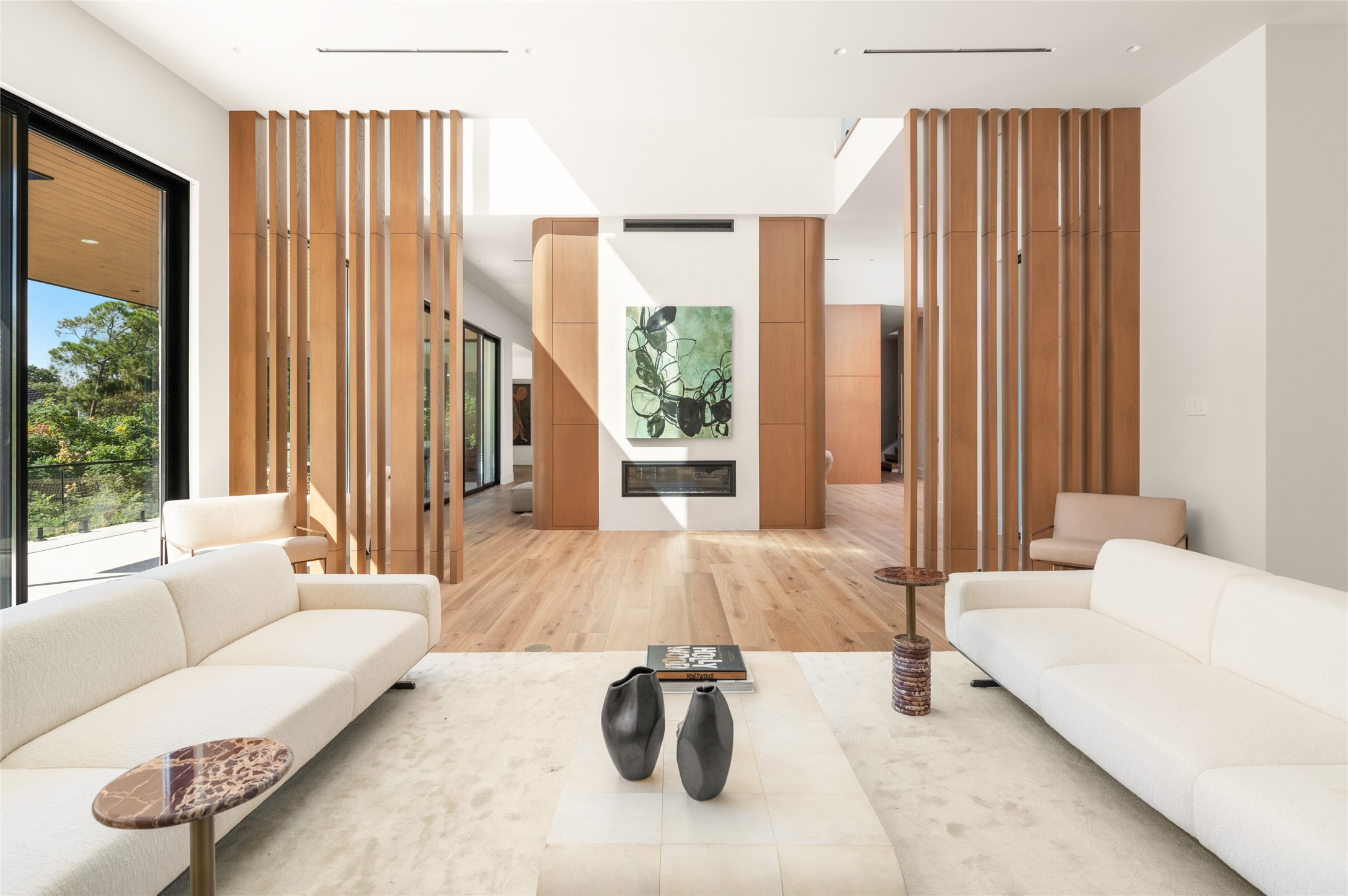 Back inside, the bar area sits just off the extended terrace and opposite the family room fireplace, with sculptural wood partitions, warm natural finishes and an open layout that connects the surrounding living spaces.