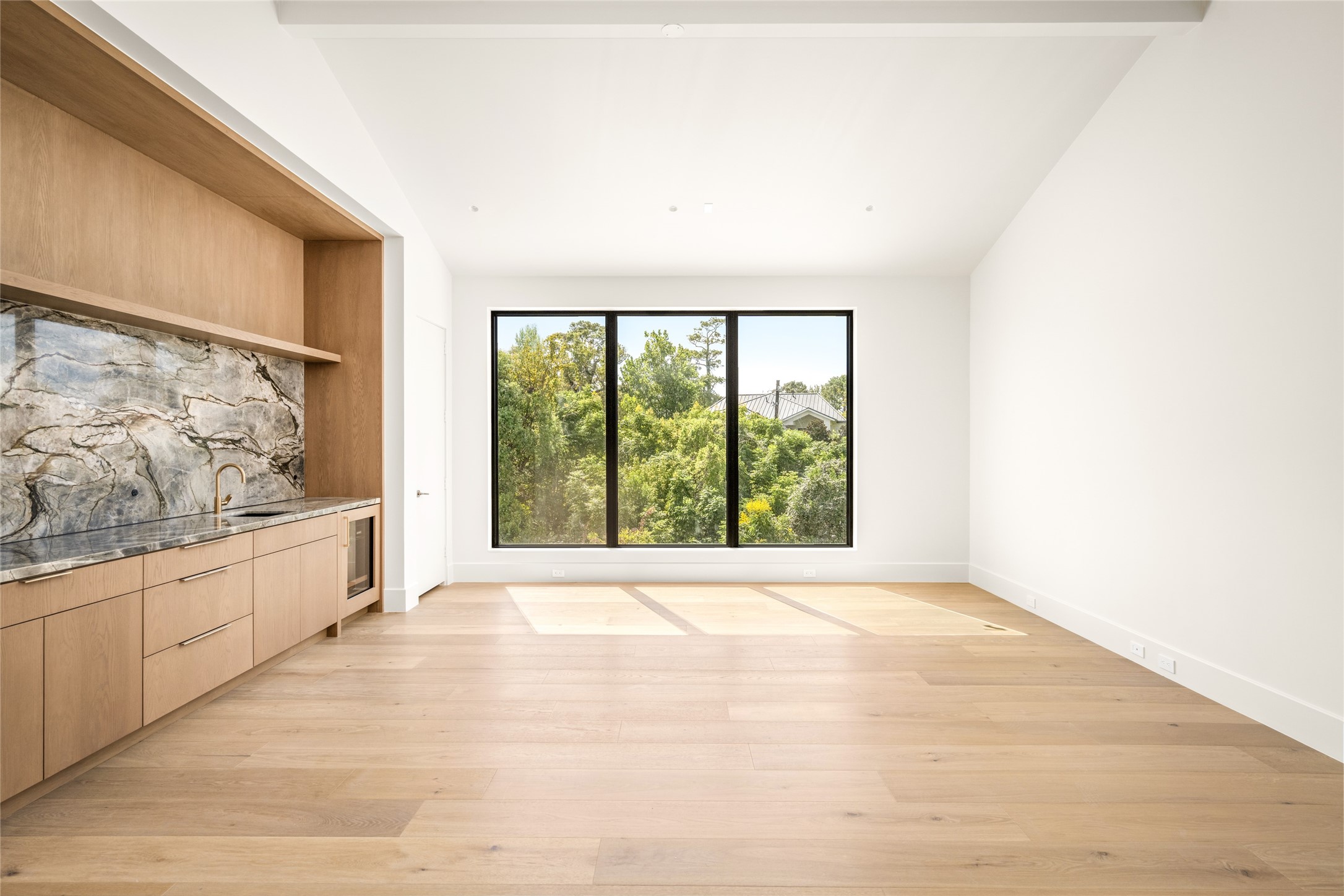 The upstairs game room offers a versatile space for relaxing or entertaining, complete with a custom wet bar featuring Blue Tempest quartzite, a beverage refrigerator, and built-in cabinetry, all complemented by beautiful treetop views.