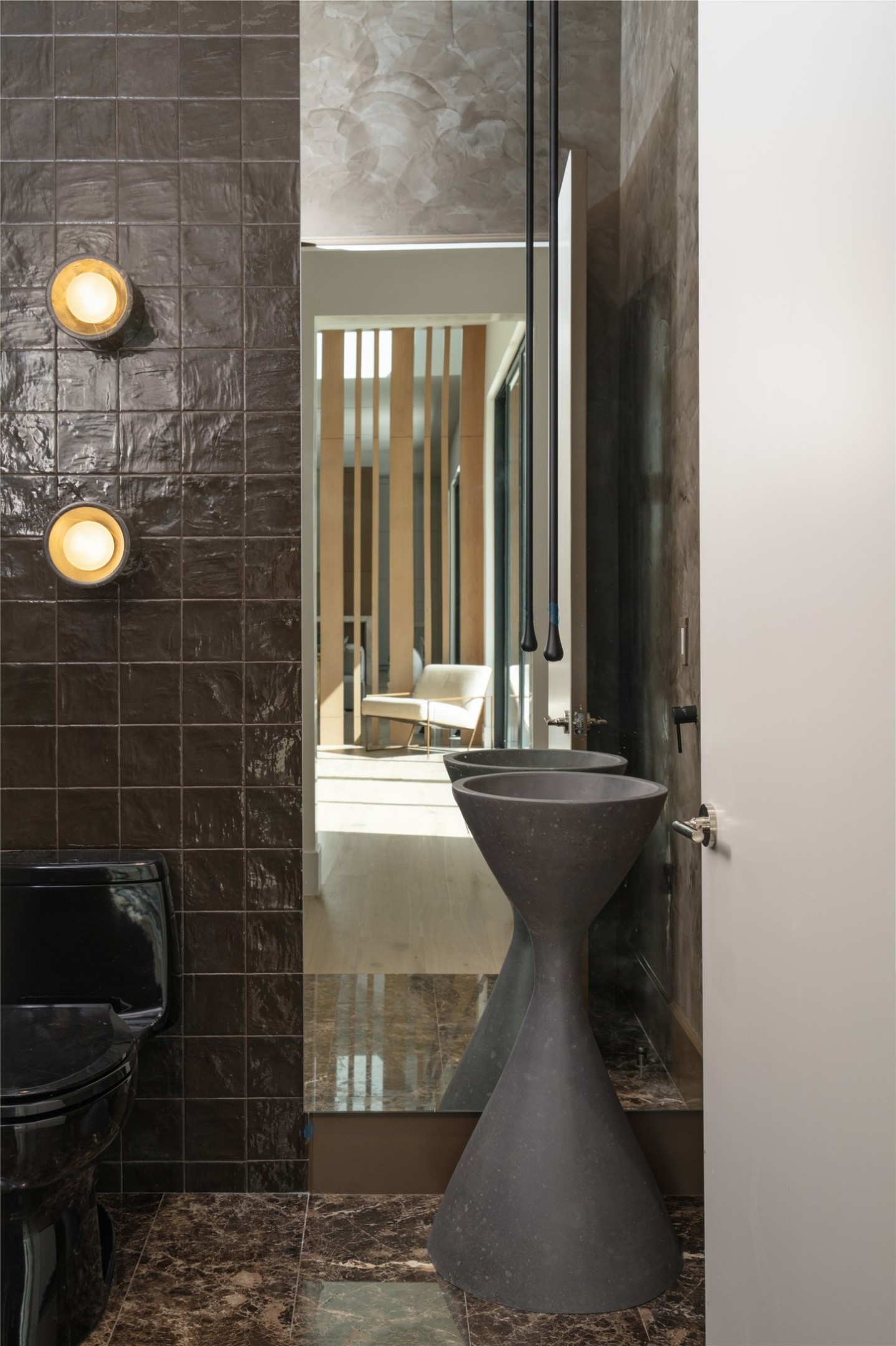 A moody, sophisticated powder room near the entertaining bar makes a bold statement with Emperador Dark marble flooring, rich cocoa Zellige tile, textured Roman clay walls, and a sculptural stone basin with a suspended glass faucet.