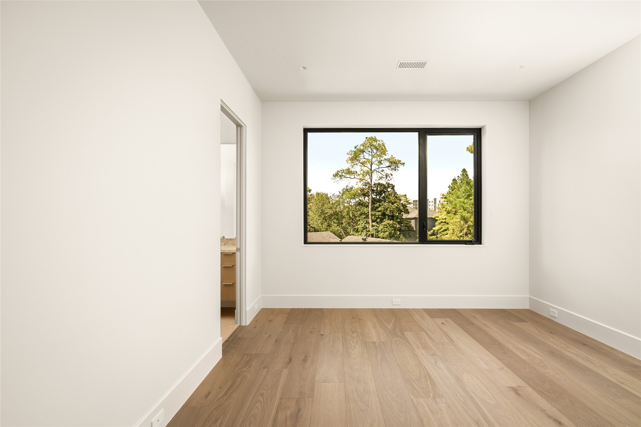 This oversized 16' x 13' bedroom suite is a bright and inviting retreat with beautiful wood floors, a clean, contemporary aesthetic, and a picturesque window overlooking mature trees.